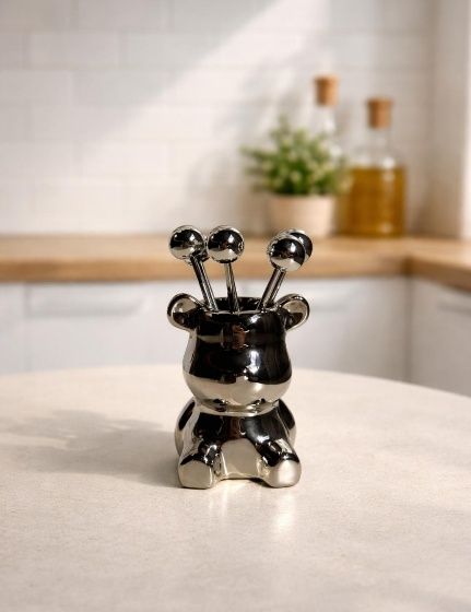 Un soporte metálico con forma de oso que contiene pequeños palillos para cócteles, colocado sobre la encimera de la cocina.