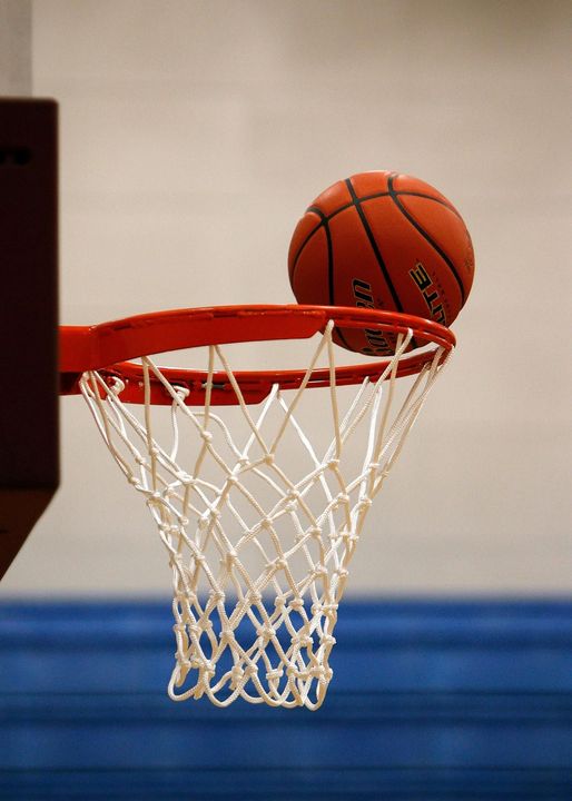 Basketball bouncing near a hoop with a white net against a blue gym wall