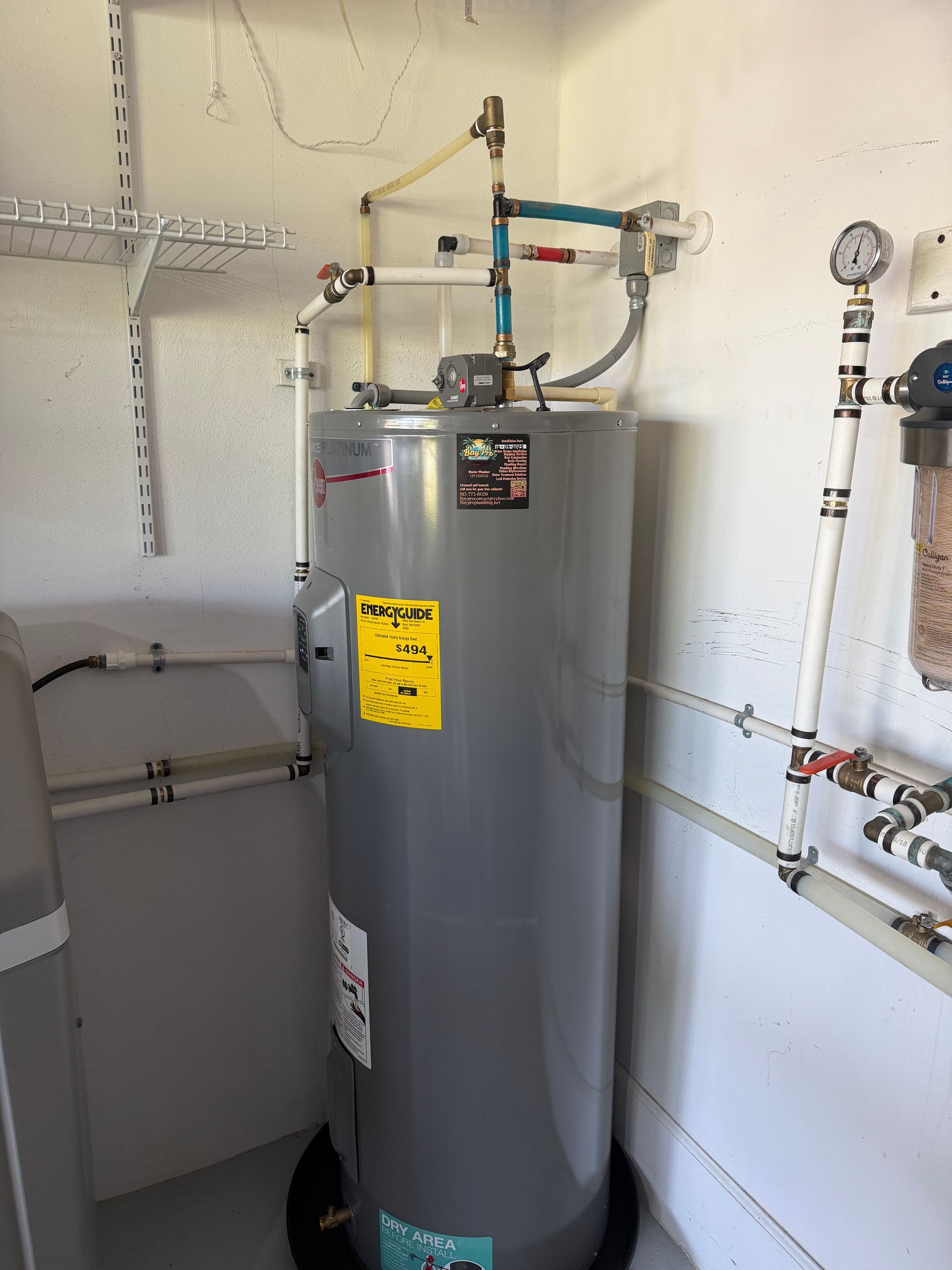 Plumber in blue overalls repairing a boiler, standing on a step stool indoors.