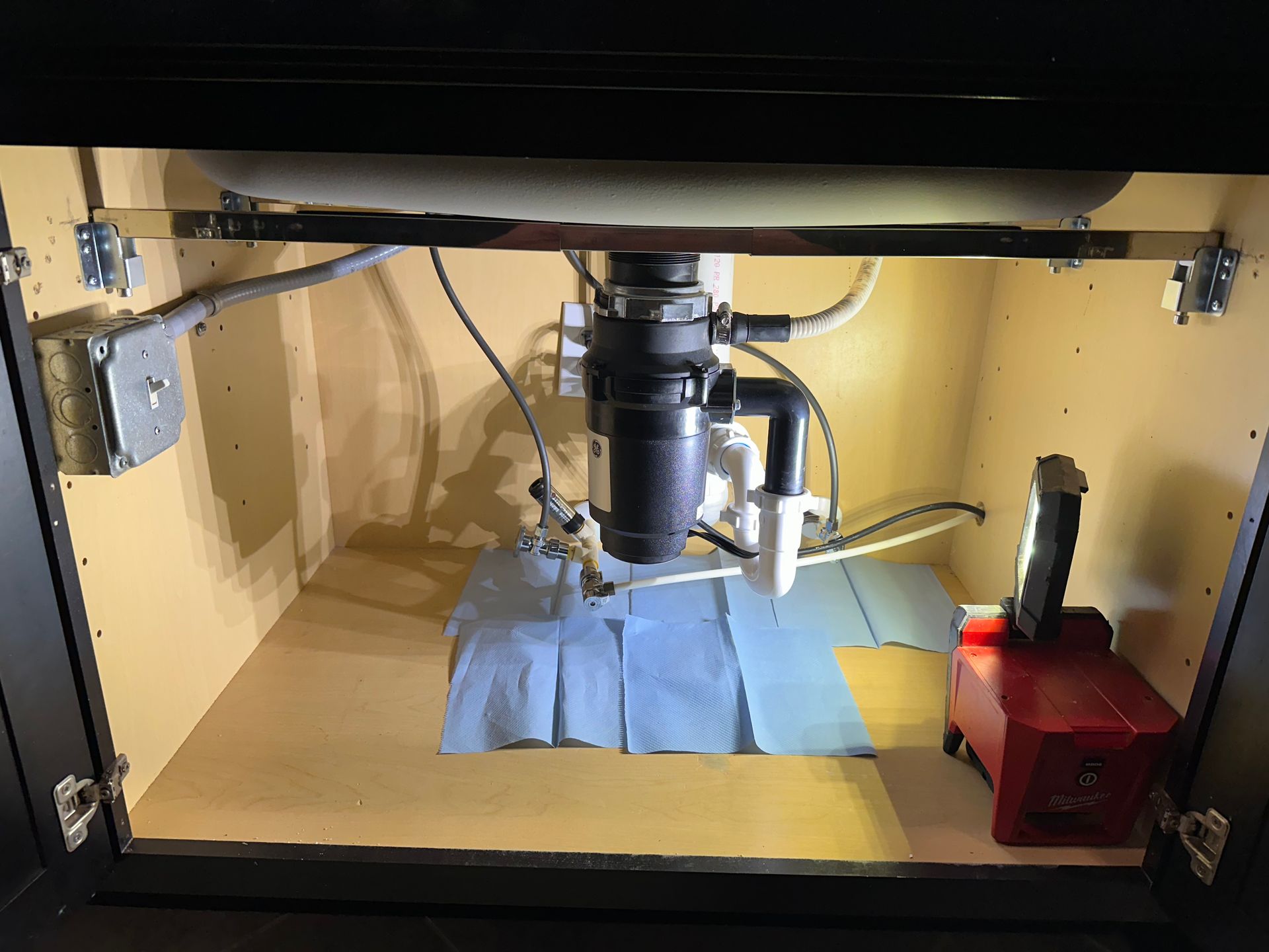 Plumber working under a kitchen sink, tools and parts visible on counter. Plumber working under a kitchen sink, tools and parts visible on counter.