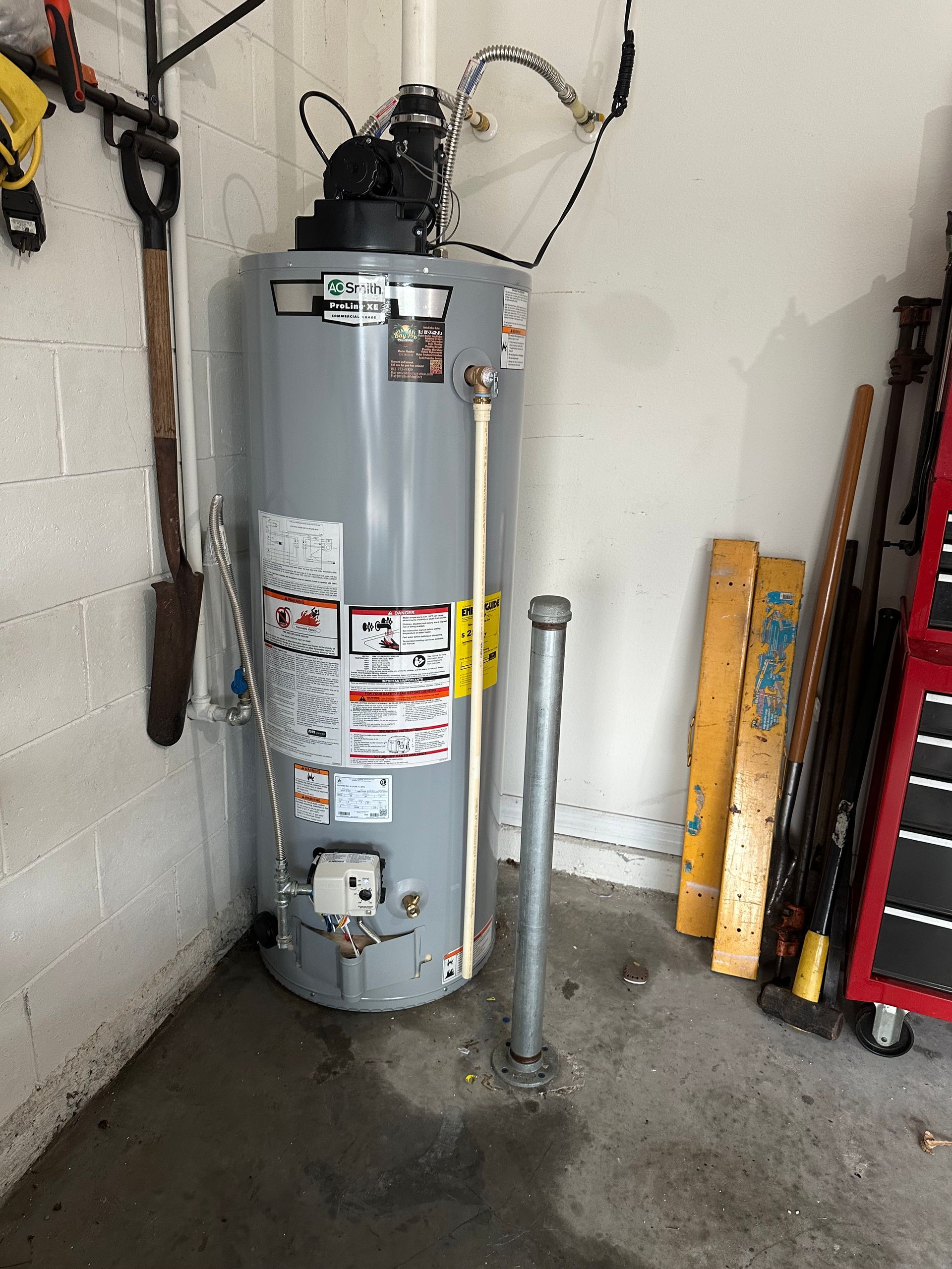 Person working on a water heater, red valve visible. Indoor setting with white walls.