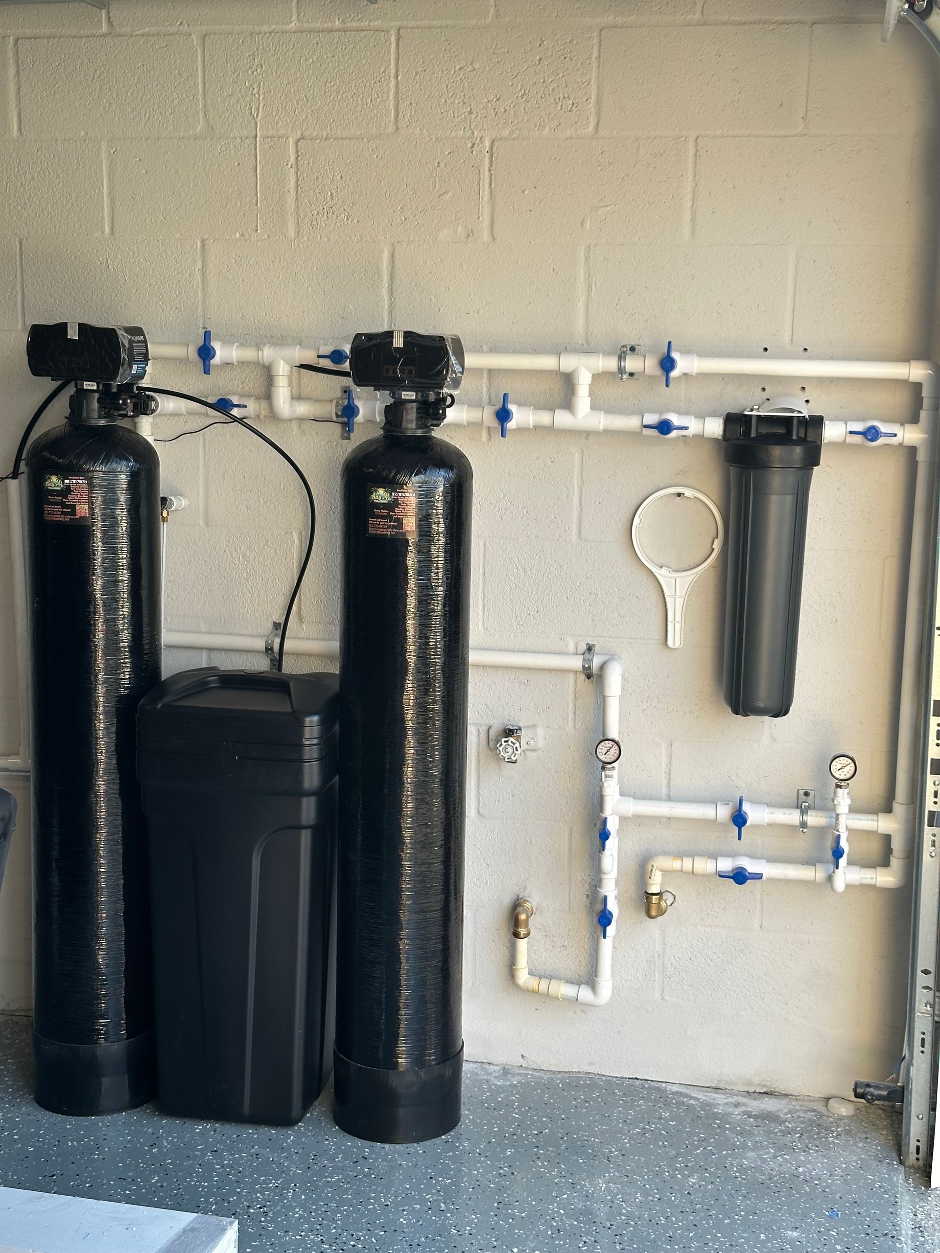 Water filtration system with electronic control panel, gray tank, and blue pipes against a wall.