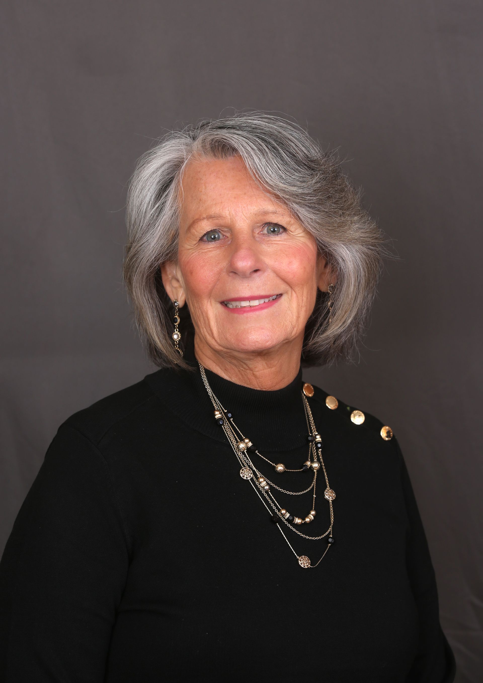 Woman with dark hair, smiling, wearing a teal top, against a white background.