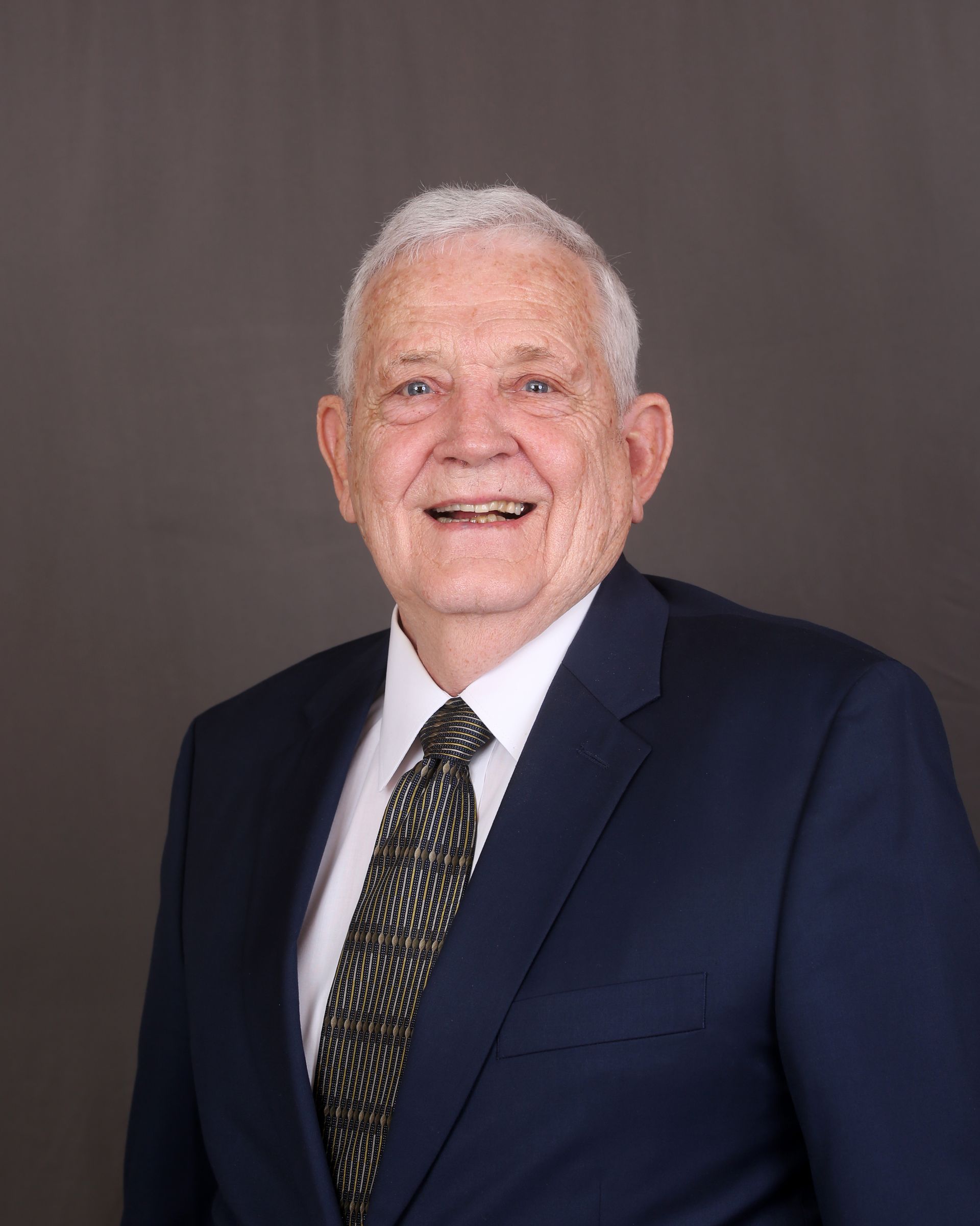 Woman with glasses, smiling, wearing a black jacket and a floral top in front of a white wall.