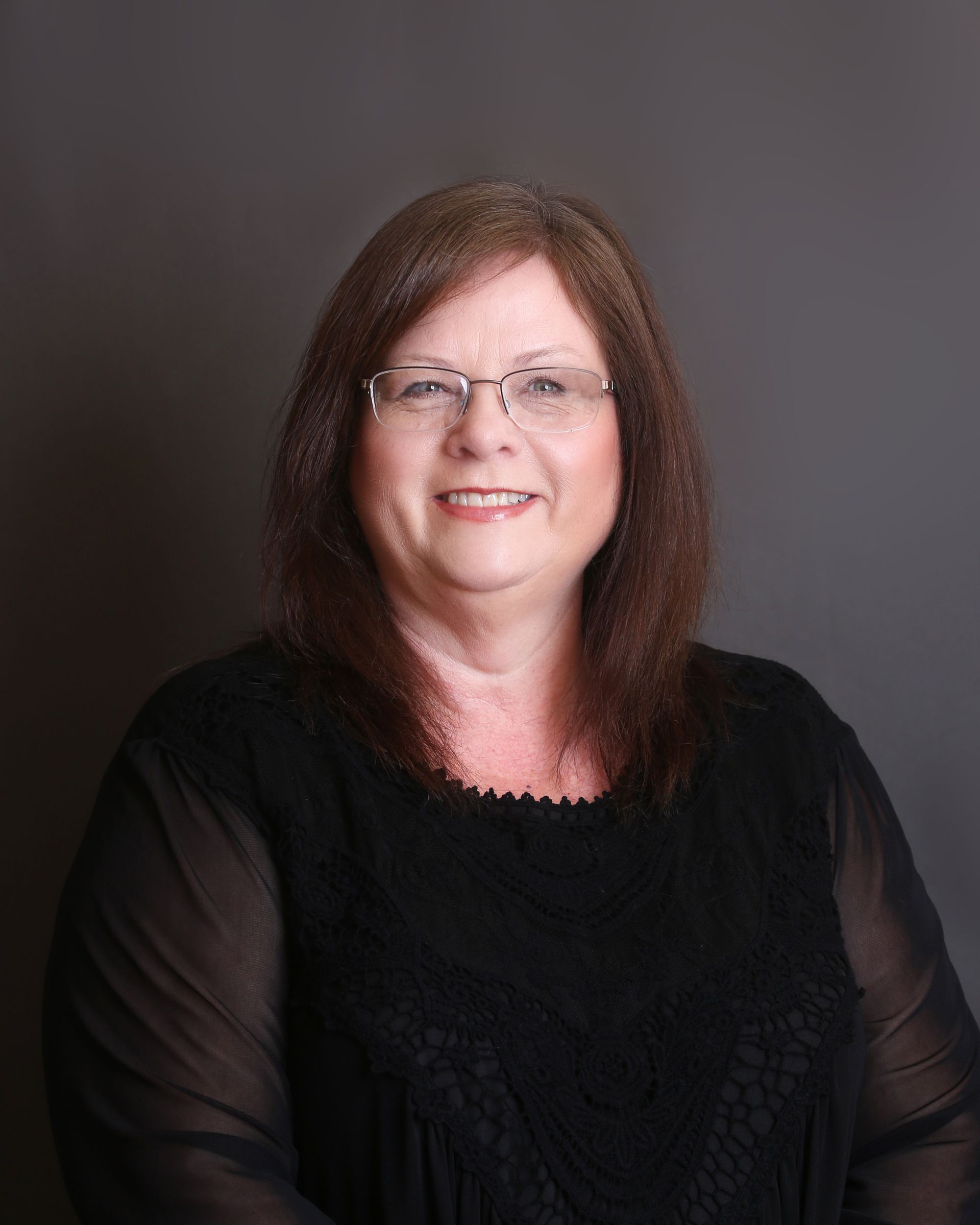 Man in dark suit smiles, head and shoulders visible against a light background.
