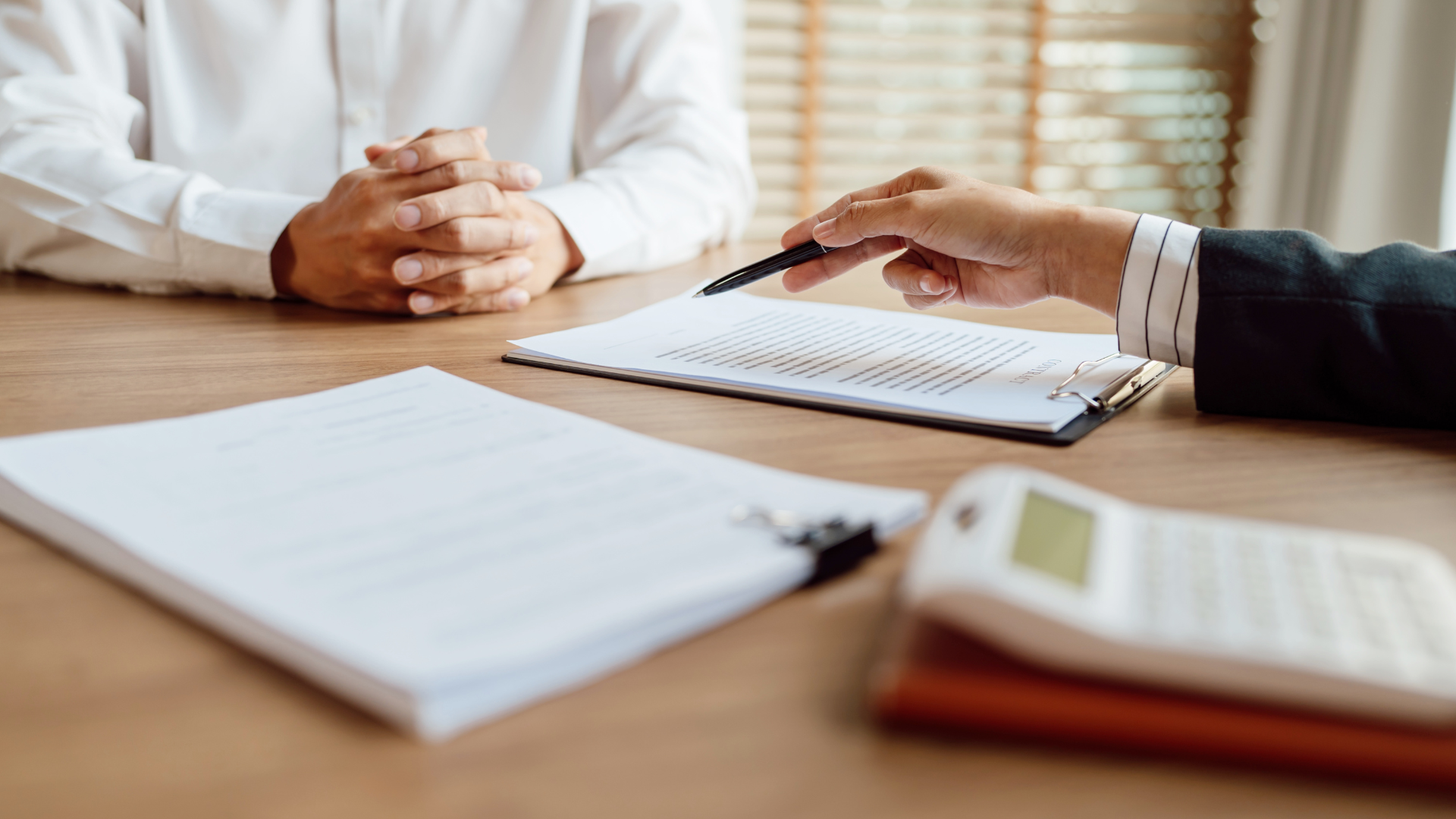 Person in white shirt at table with a hand pointing at a document, next to a calculator.
