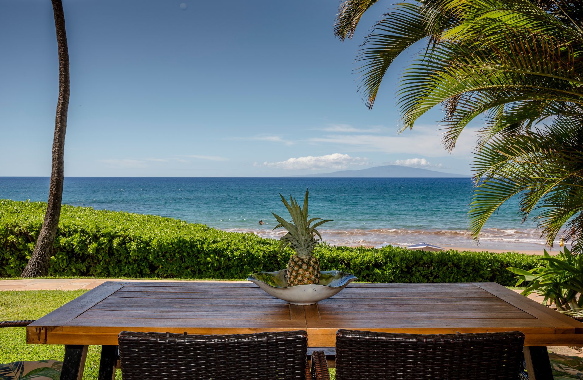 Wooden table with pineapple on a beach overlooking ocean under a blue sky.