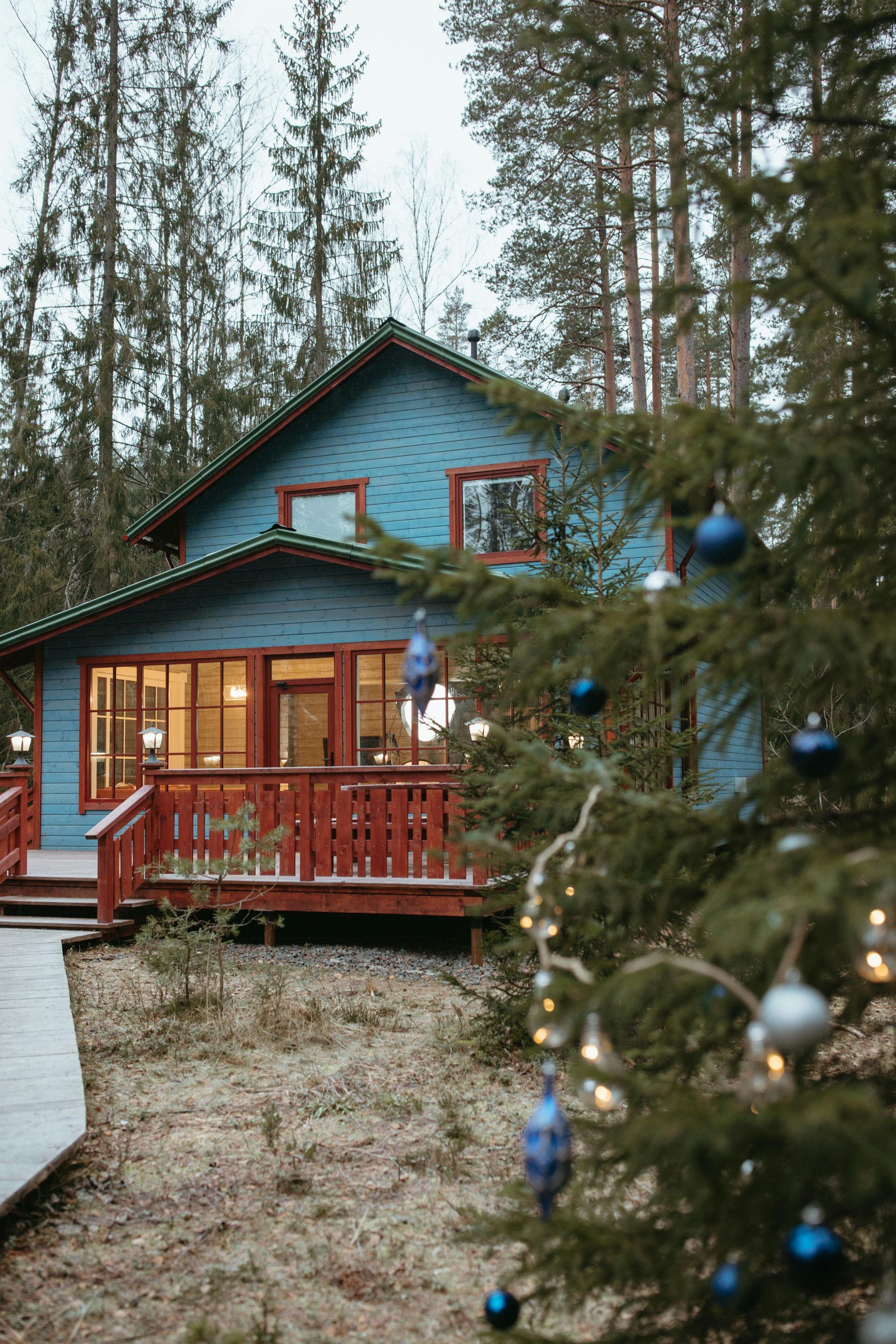 Blue cabin with red trim surrounded by trees, decorated for the holidays.