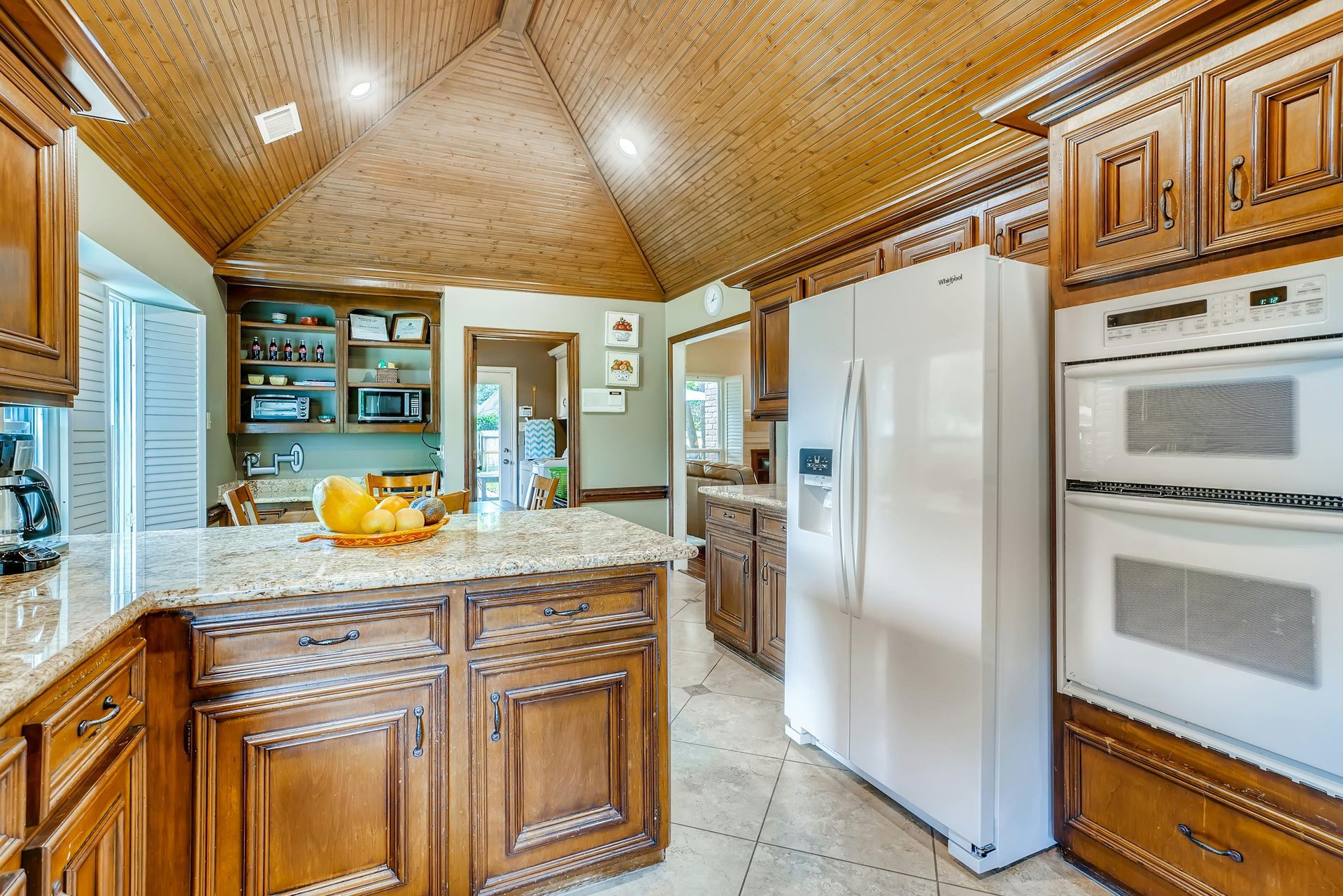 Kitchen with wood cabinets, island, granite countertop, white appliances, and a vaulted ceiling.