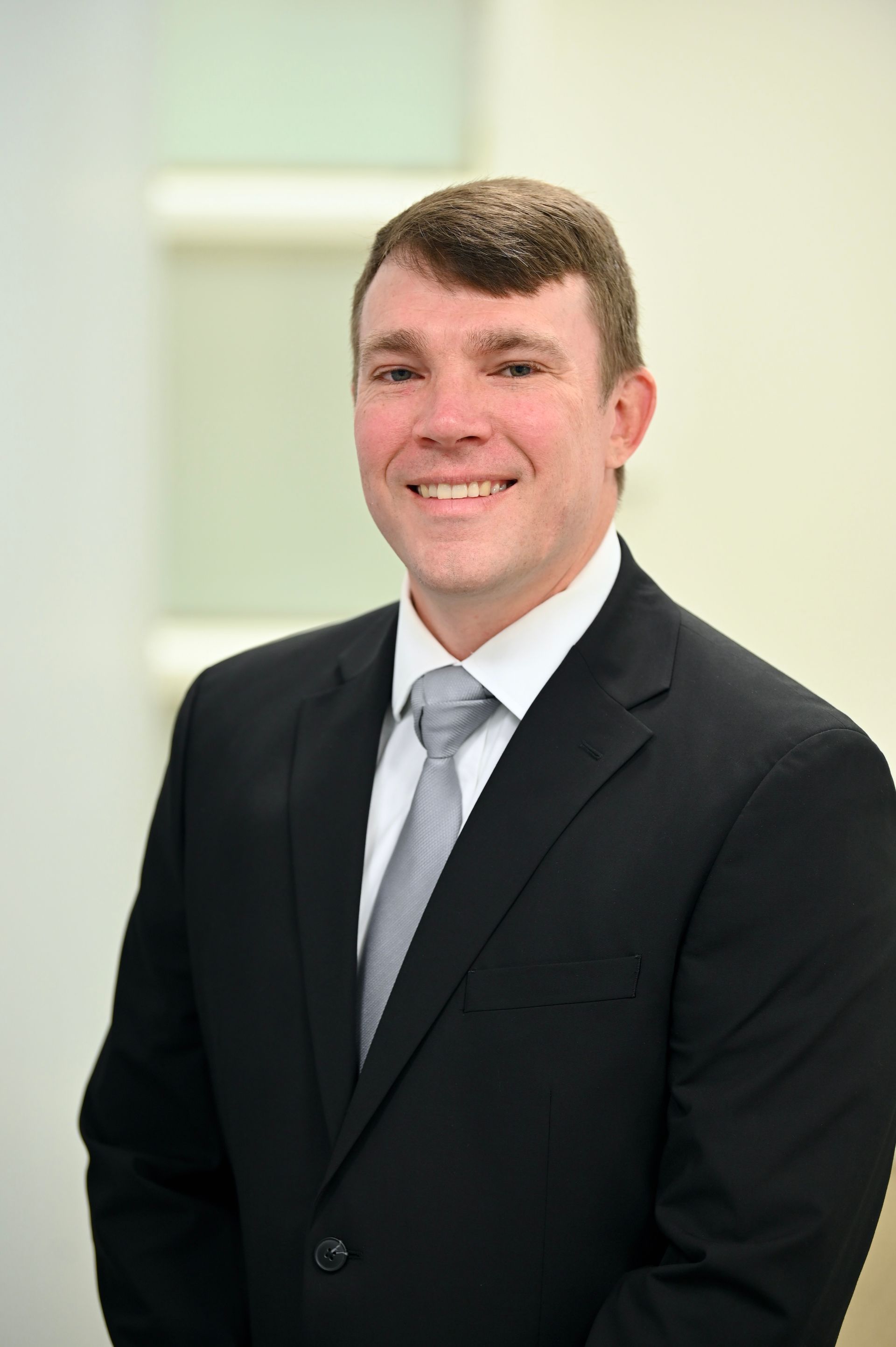 Man in black suit and tie, smiling, in a bright office setting.