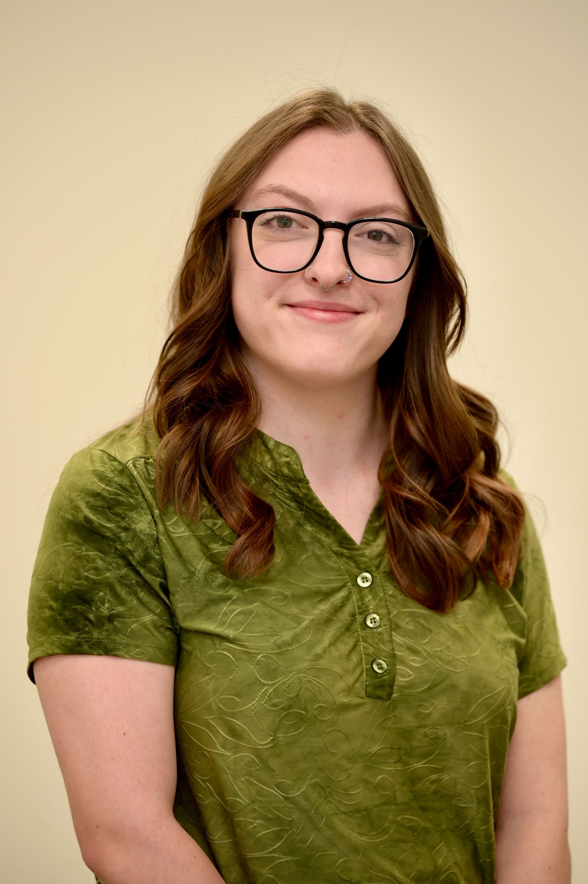 Woman with glasses in a green shirt smiles at the camera against a light background.