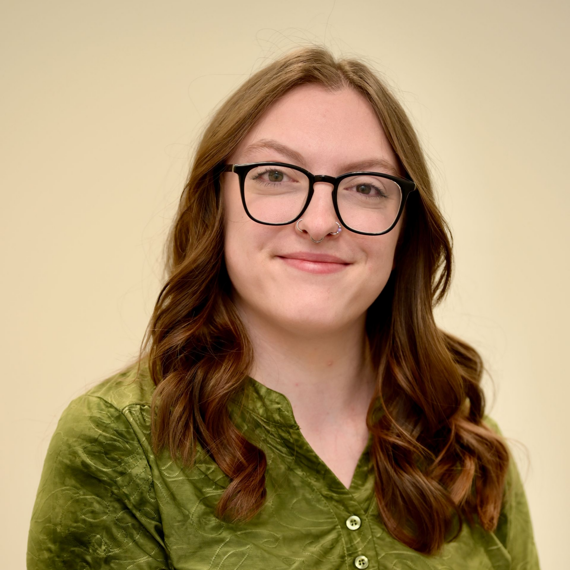 Woman with glasses in a green shirt smiles at the camera against a light background.