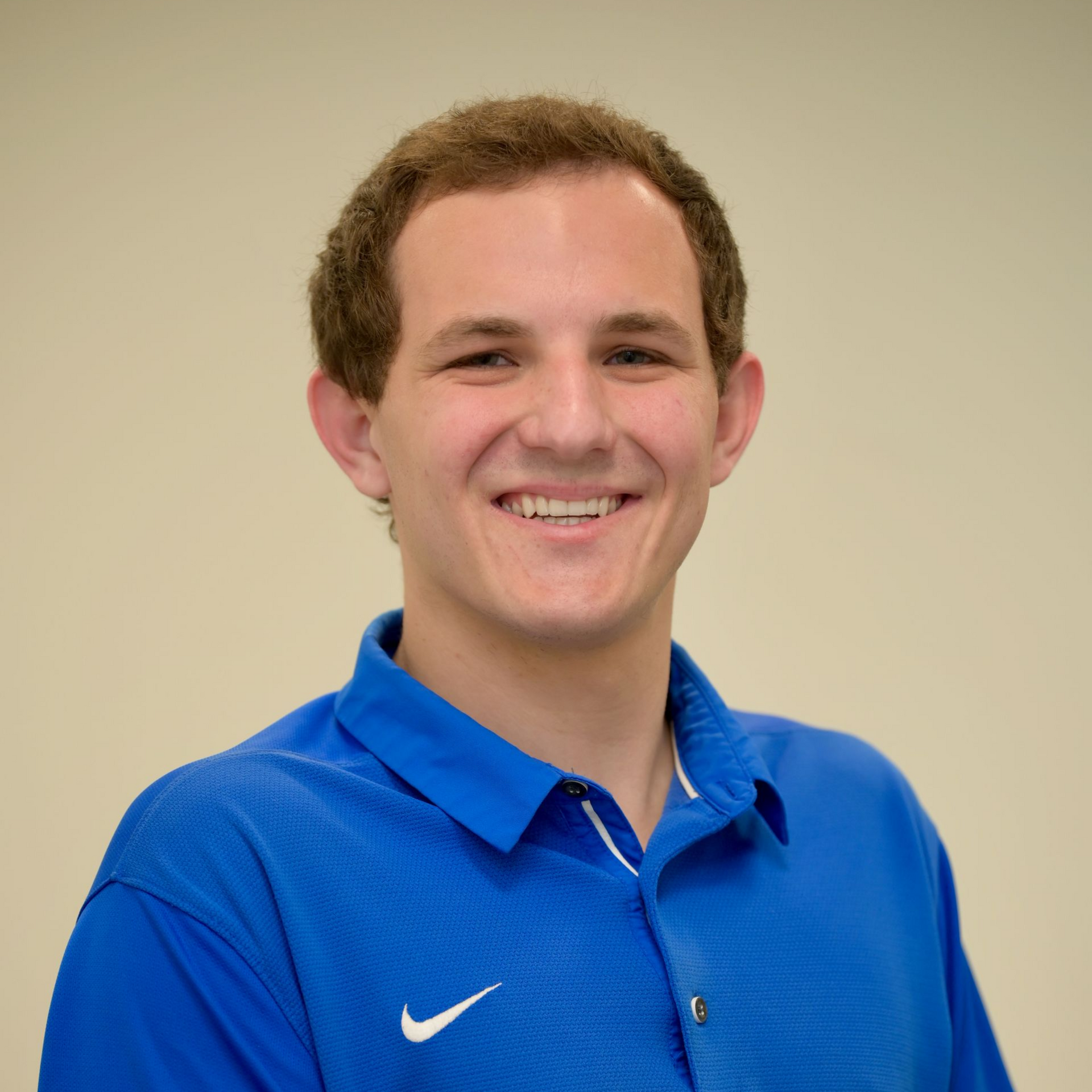 Man in blue polo shirt smiles, posing against a light background.