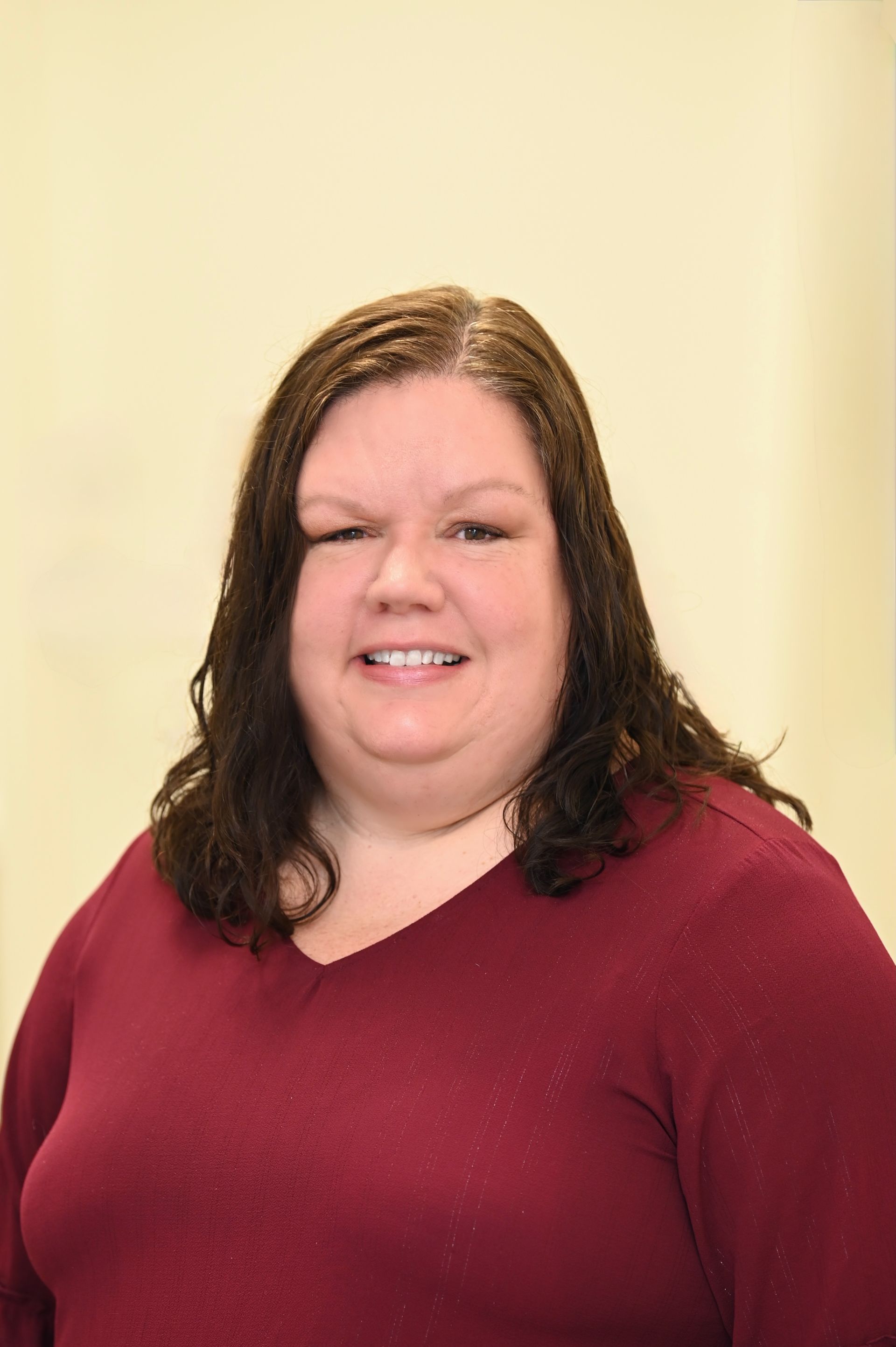 Woman with dark hair smiles, wearing a burgundy v-neck sweater, in front of a plain background.