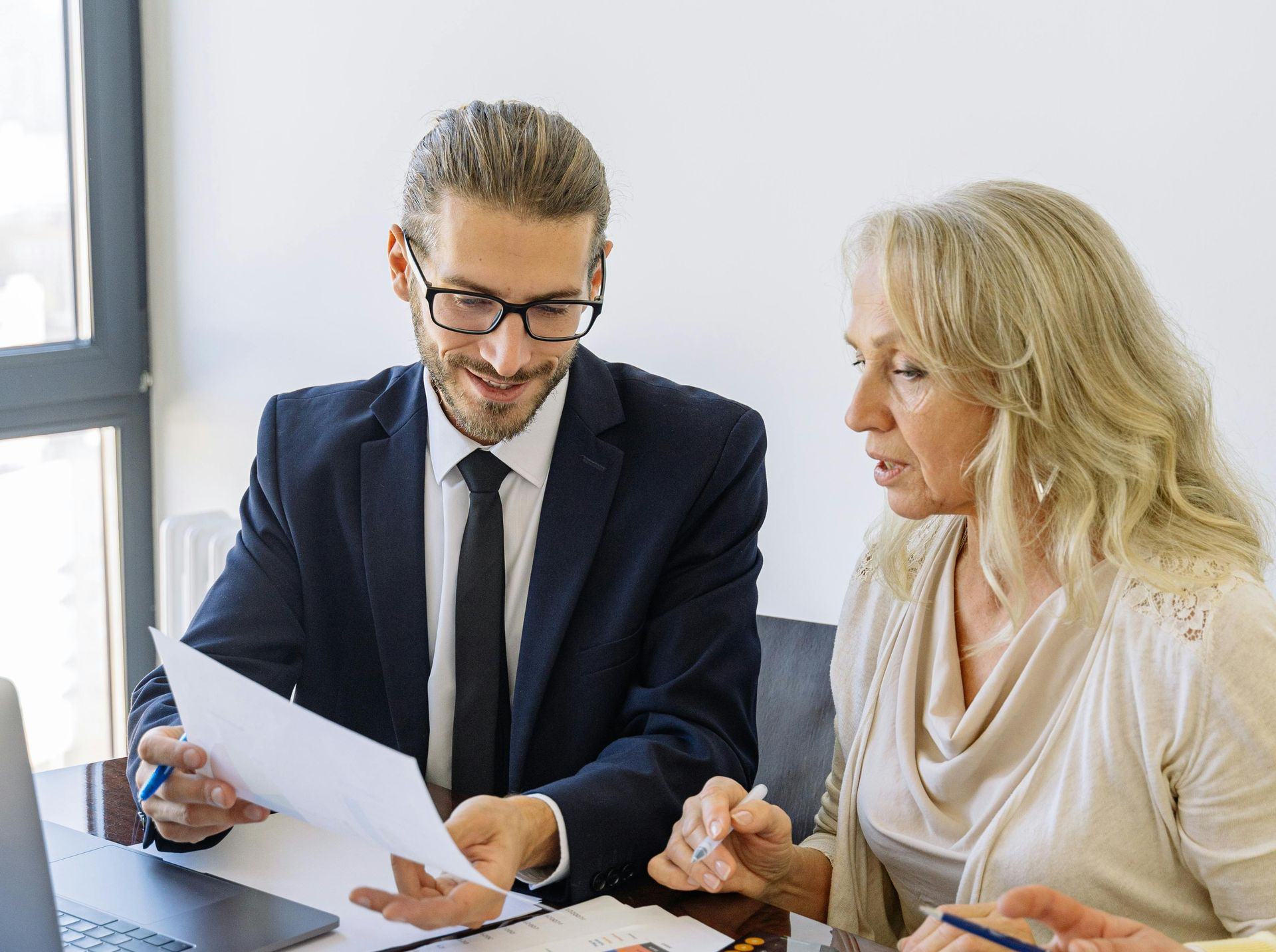 Man in suit reviews papers with woman in beige top, office setting.