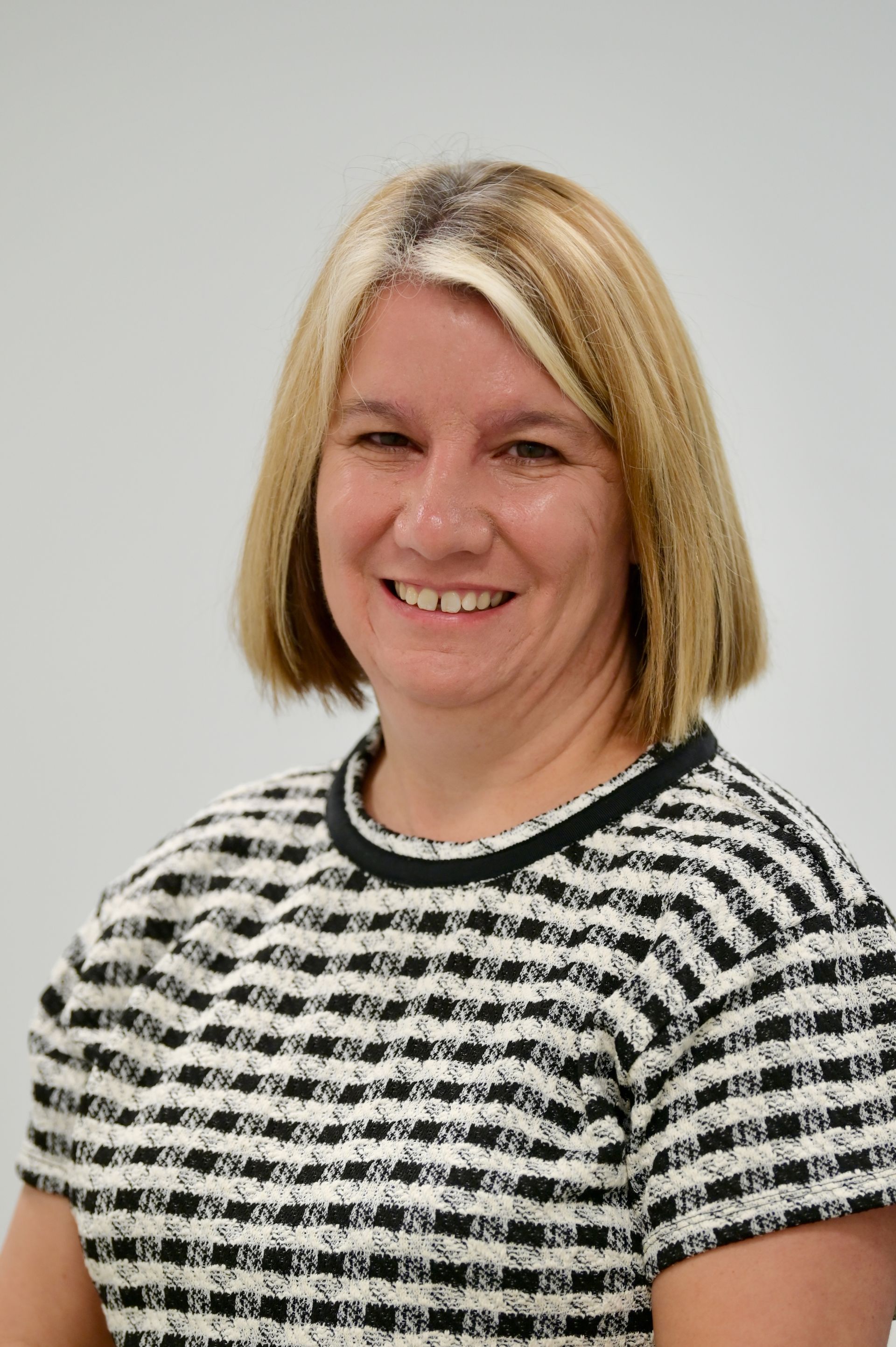 Woman with blonde hair and a black and white patterned top smiles at the camera.