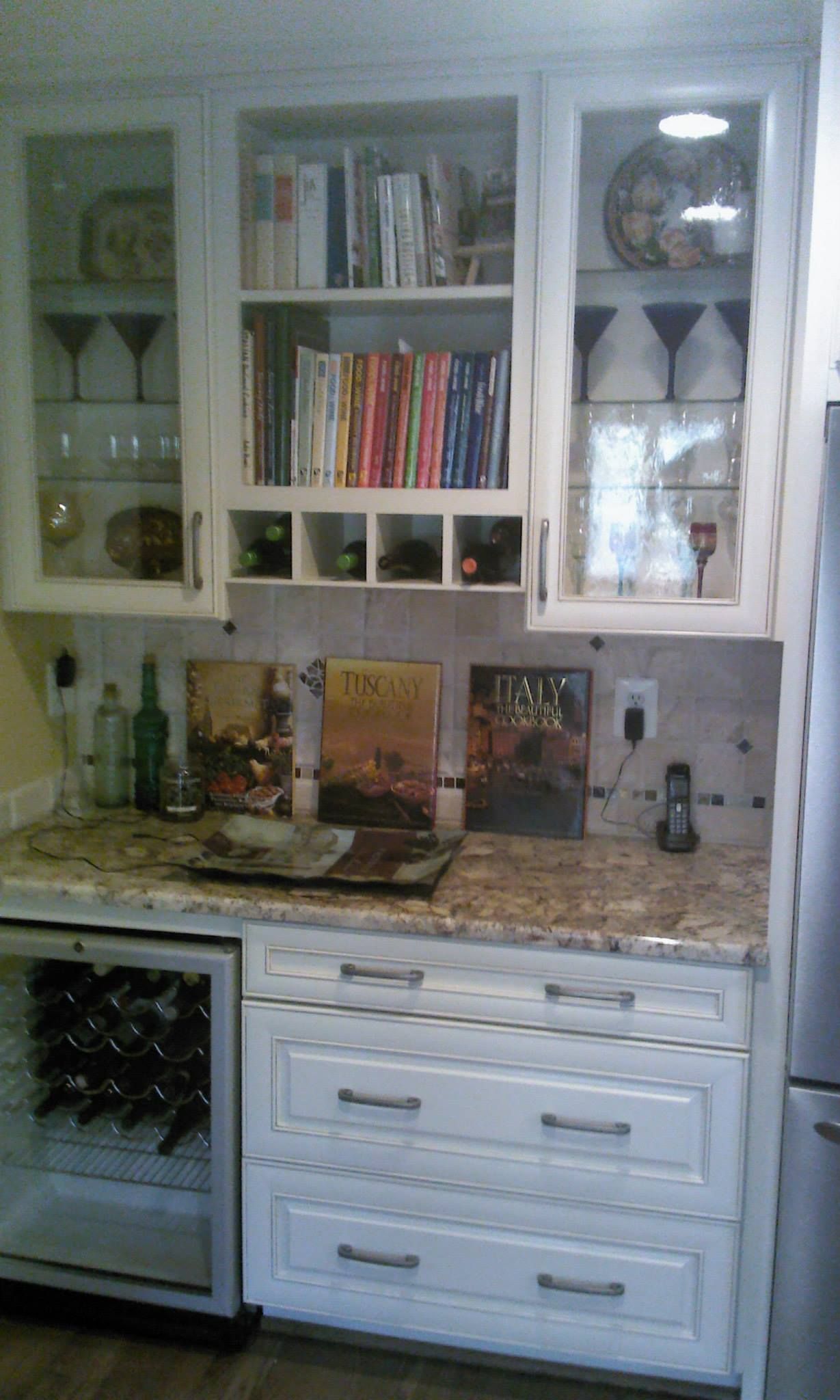 A kitchen with white cabinets , granite counter tops , and a wine cooler.