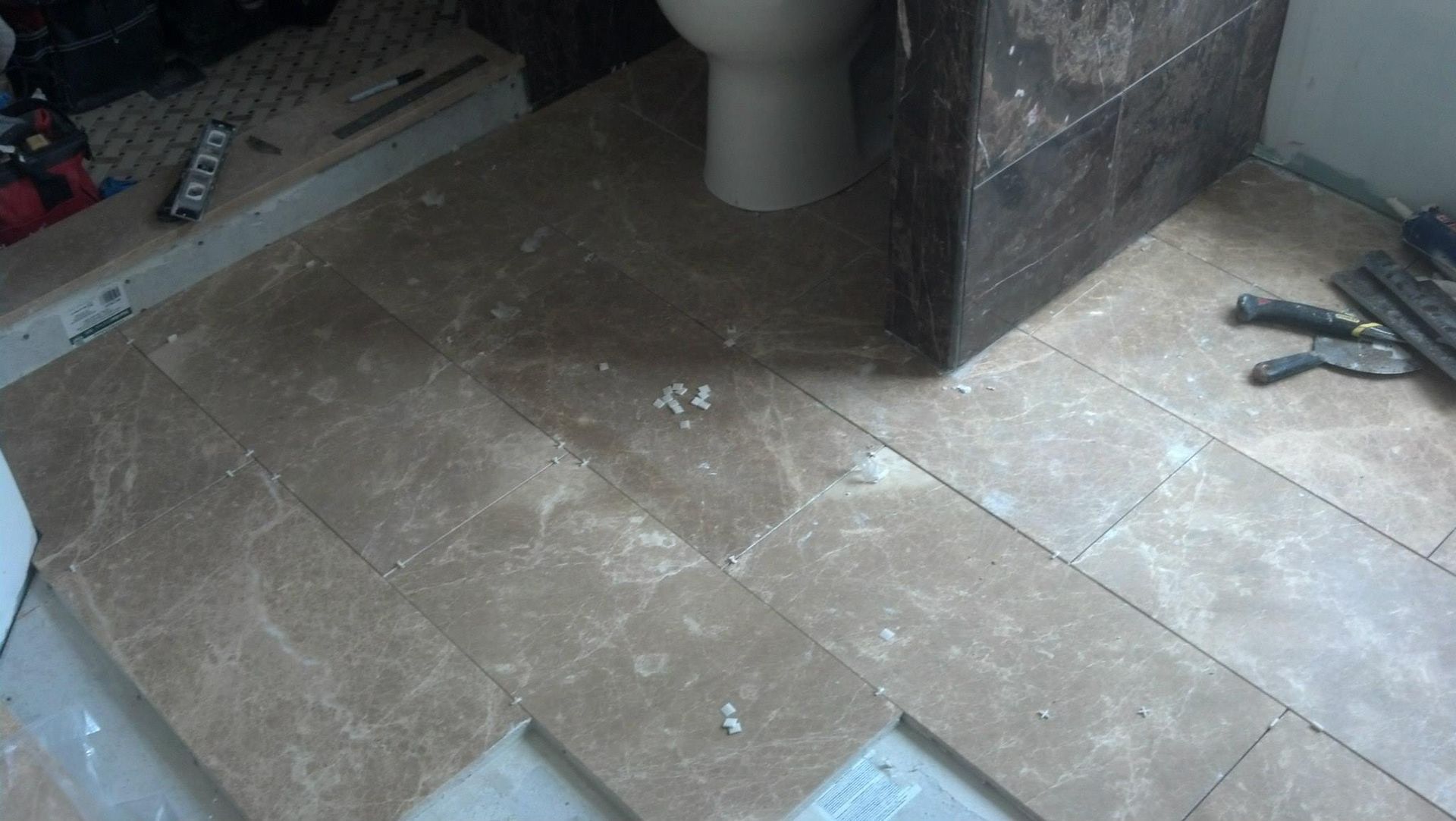 A bathroom floor with tiles and a toilet in the background.