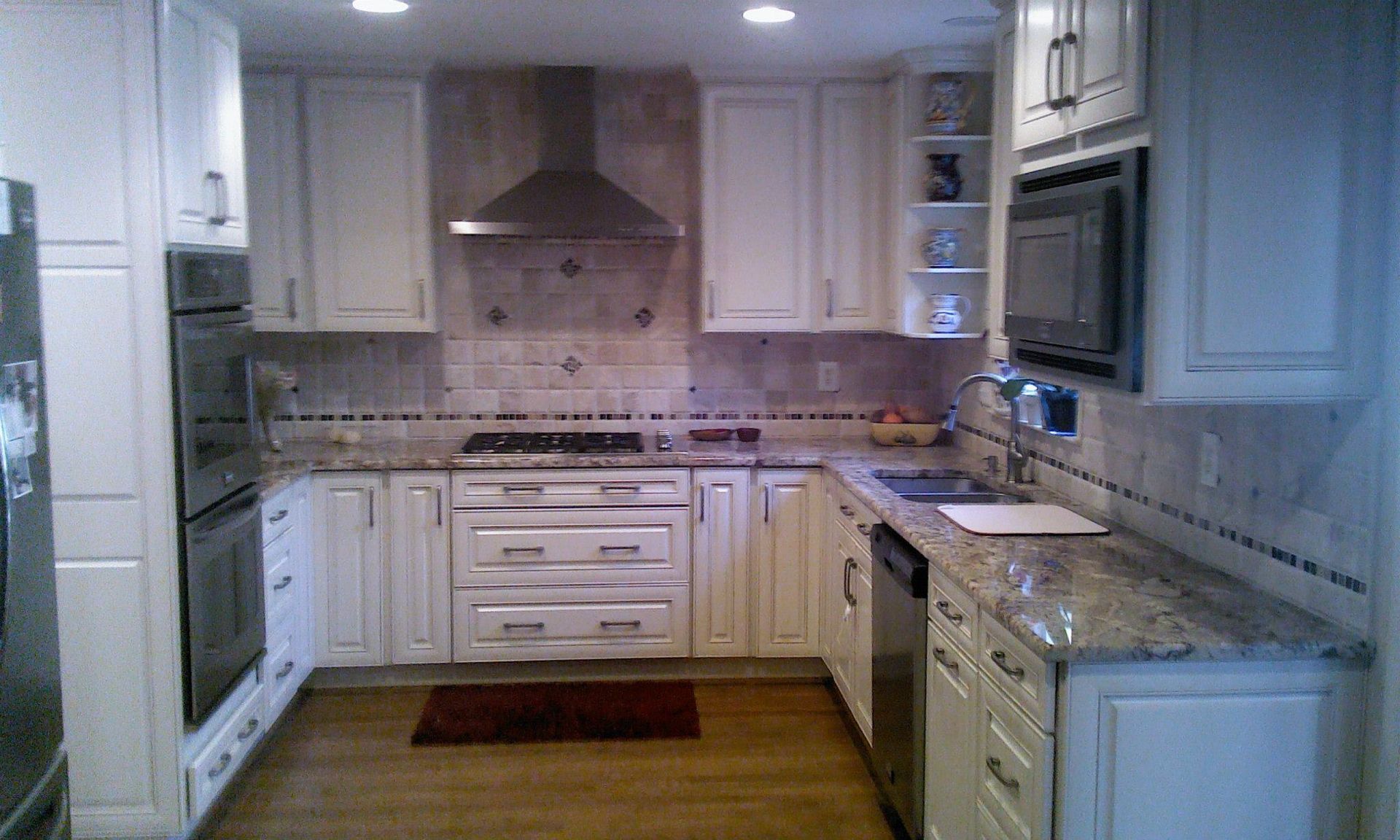 A kitchen with white cabinets , granite counter tops , stainless steel appliances and a stove.
