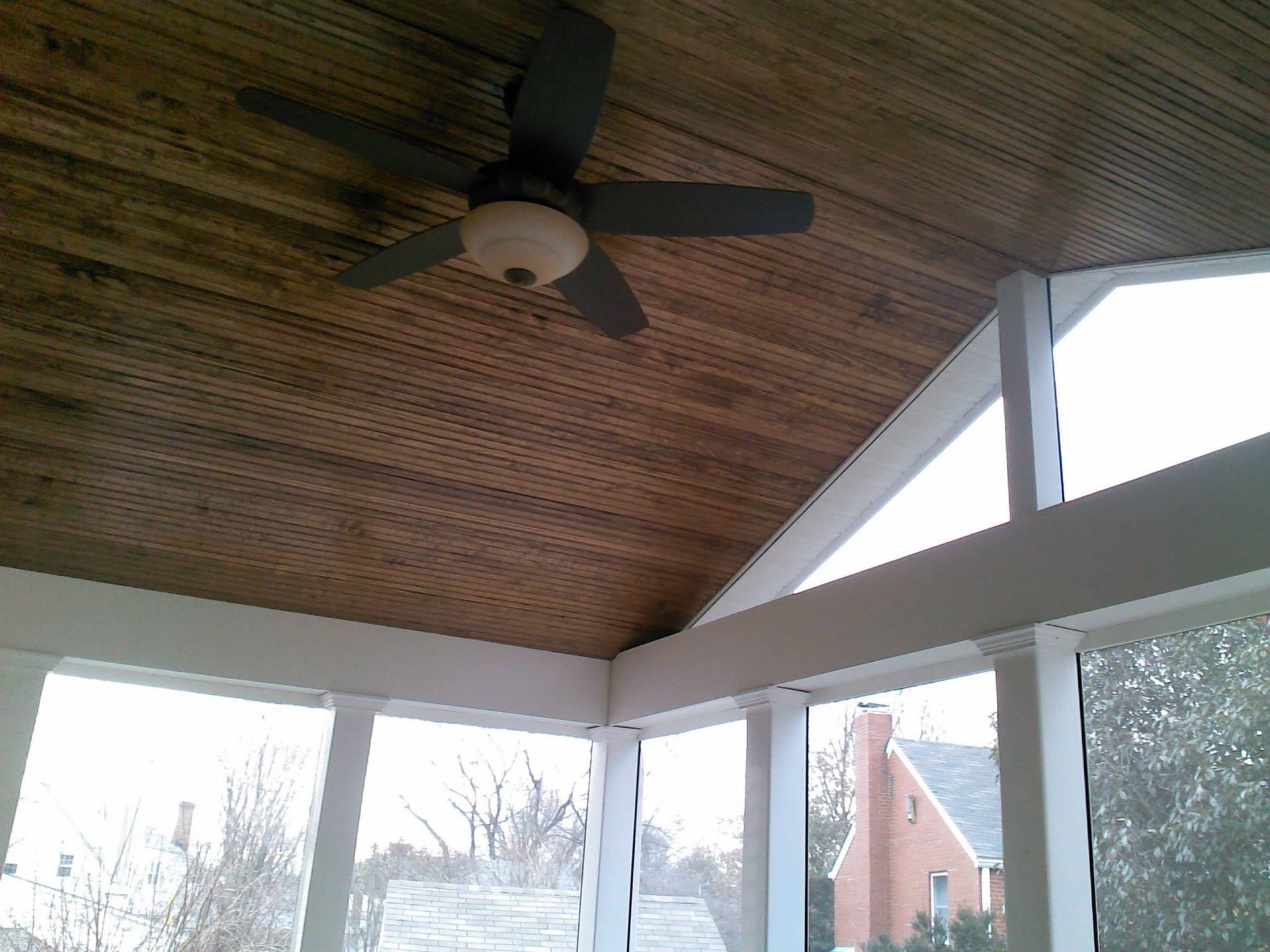 A screened in porch with a wooden ceiling and a ceiling fan