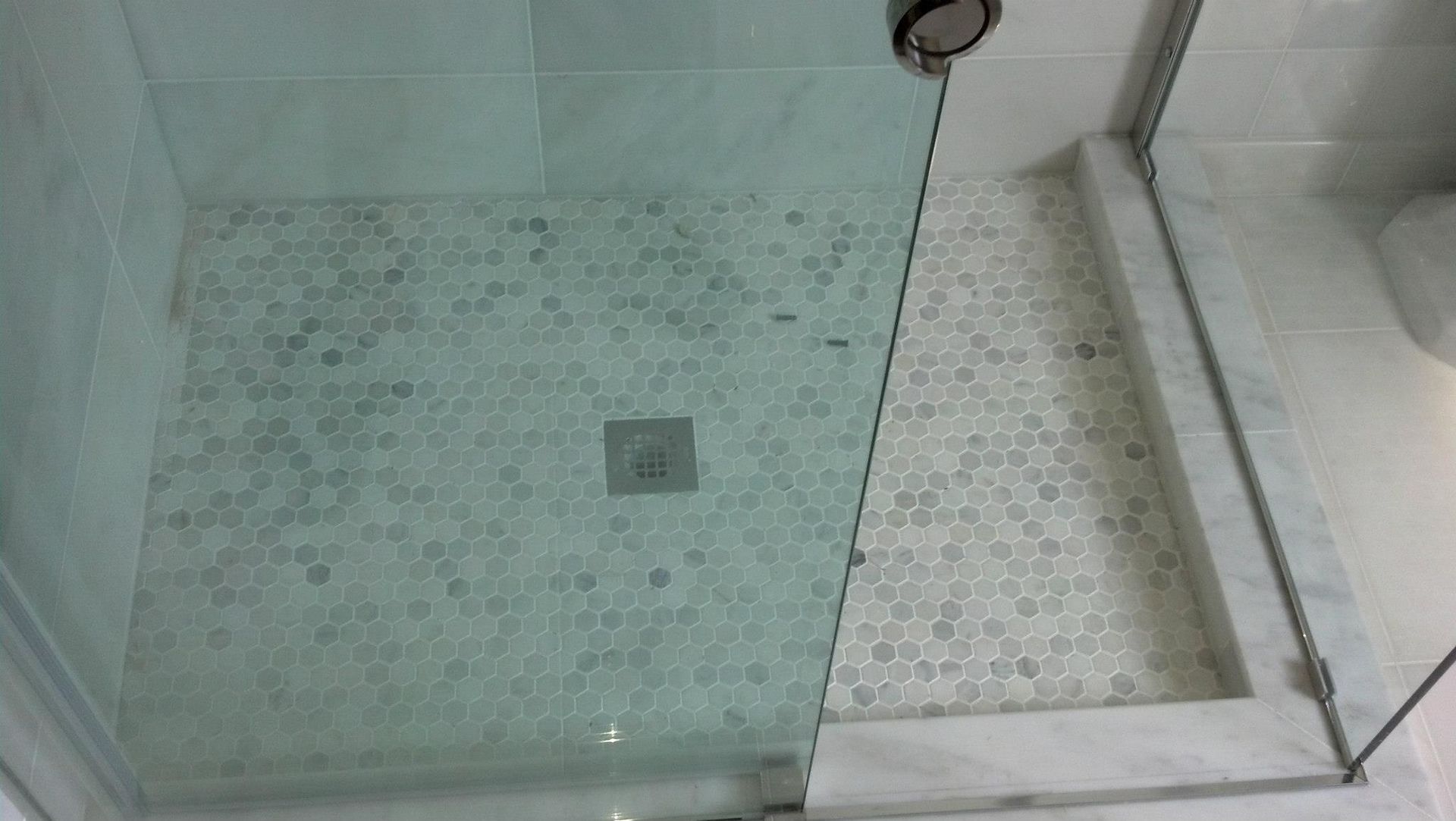 A shower stall with a glass door and a tiled floor in a bathroom.