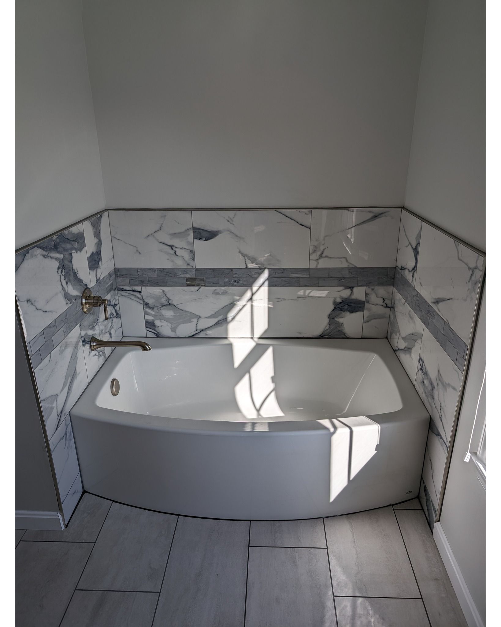A bathtub in a bathroom with marble tiles on the wall.