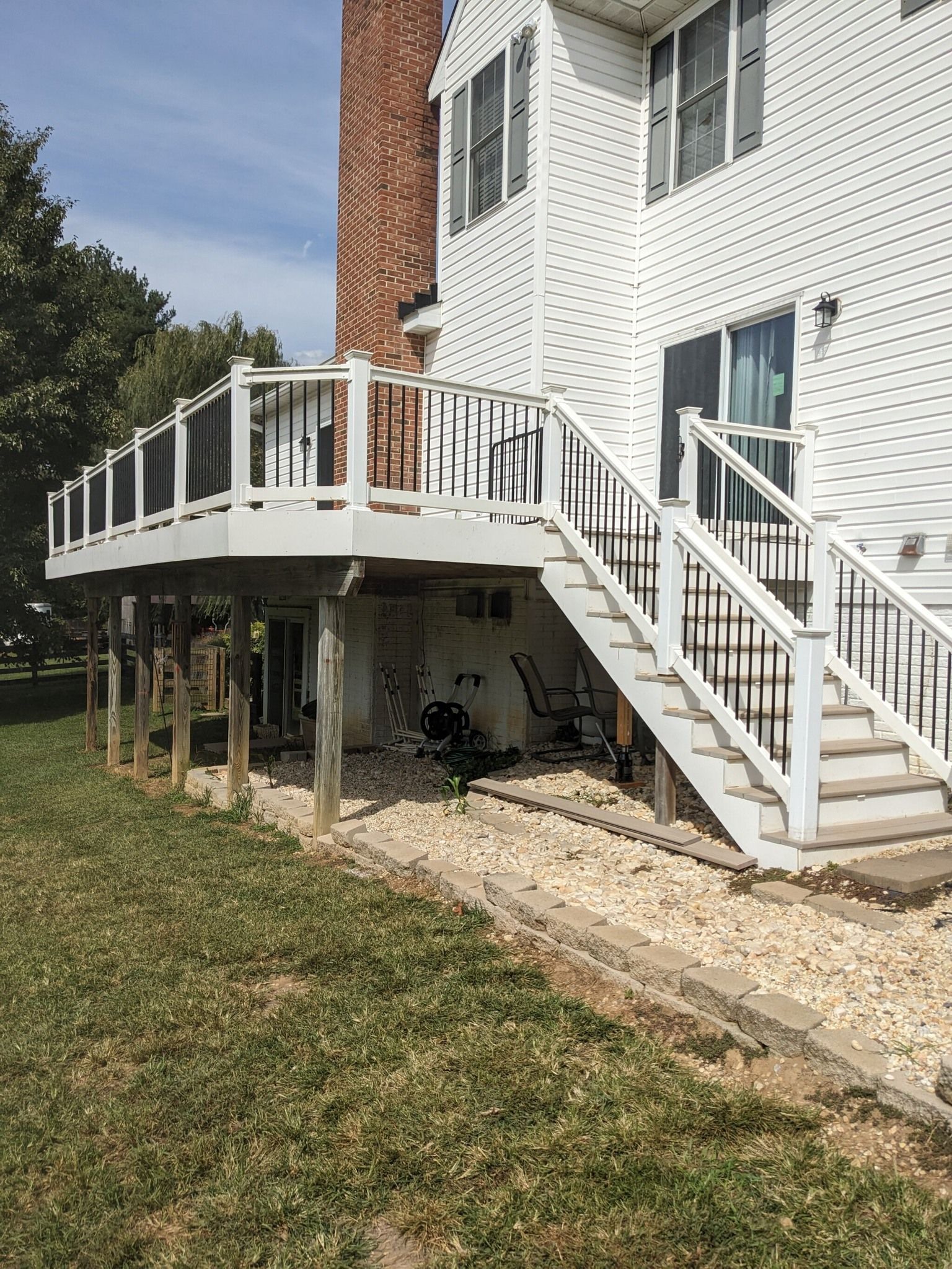 A white deck with stairs leading up to it is in the backyard of a house.