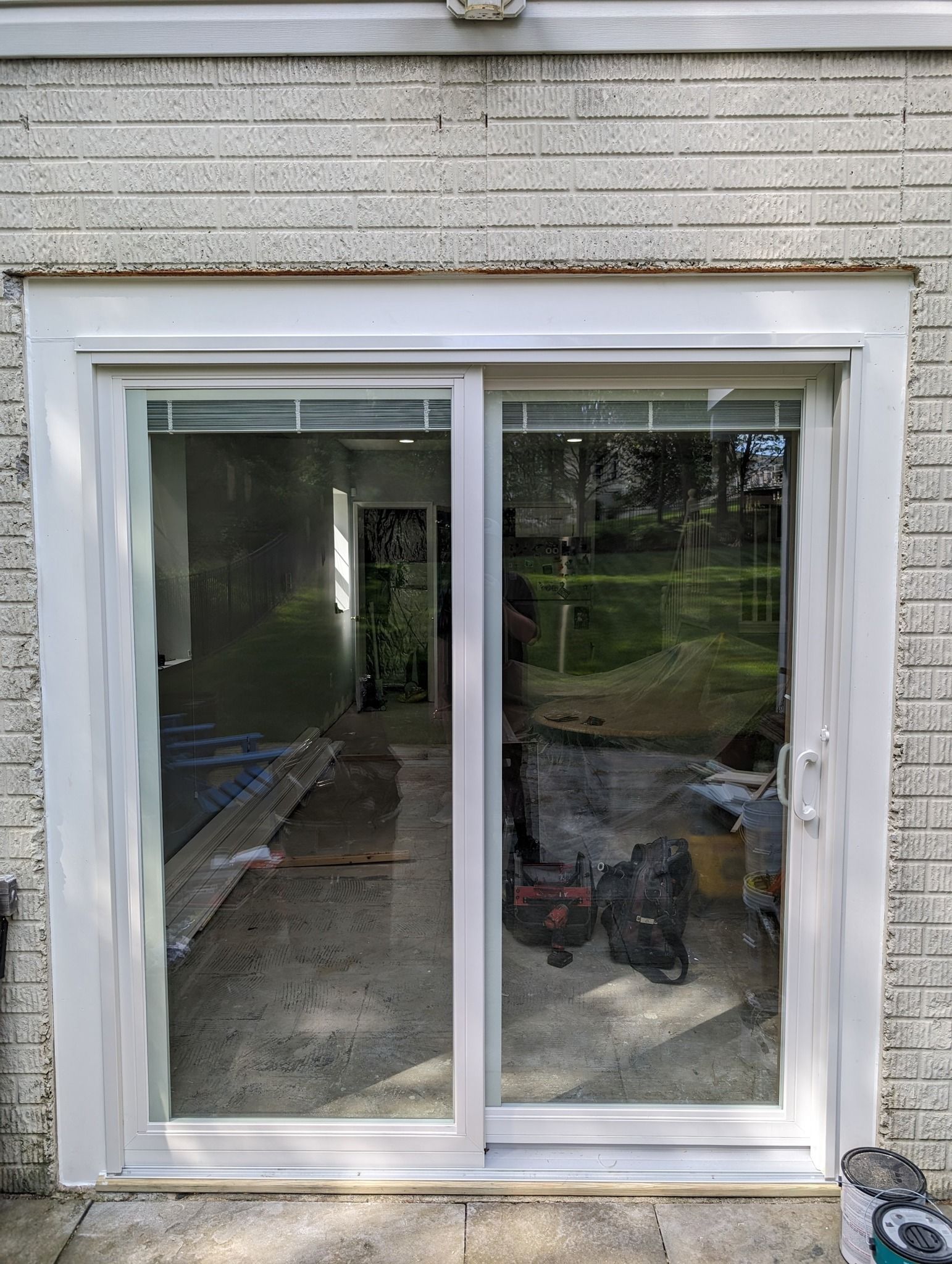 A white sliding glass door is being installed on a brick wall.