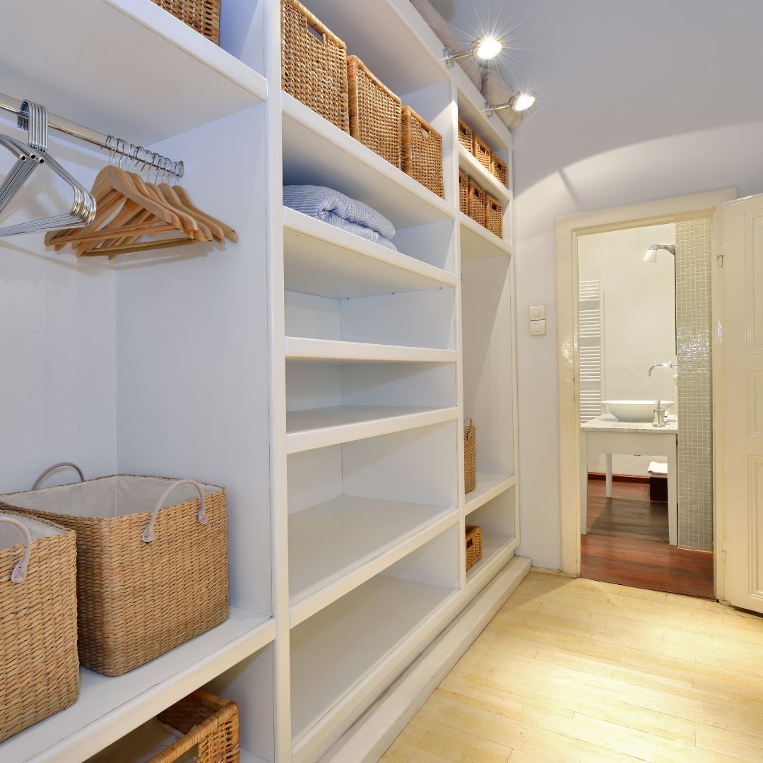 A walk in closet with wicker baskets on the shelves