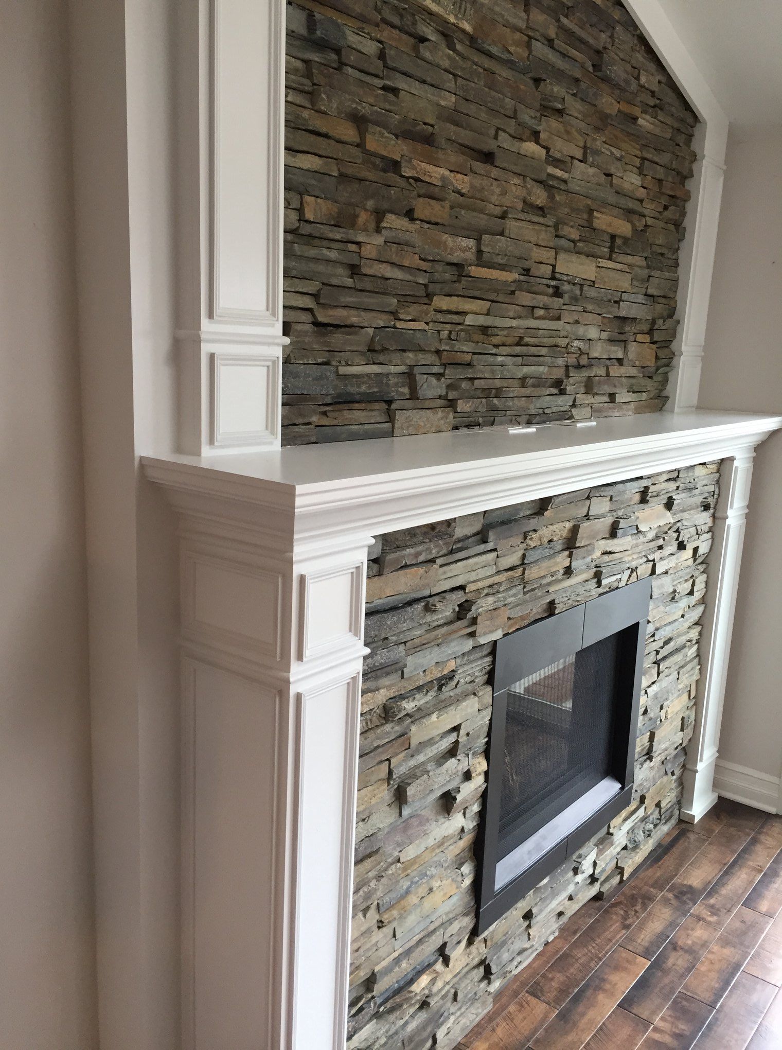 A fireplace with a stone wall and a white mantle in a living room.