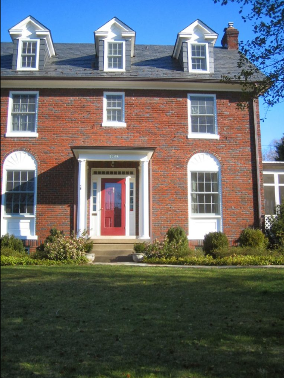 A brick house with a red door and white windows