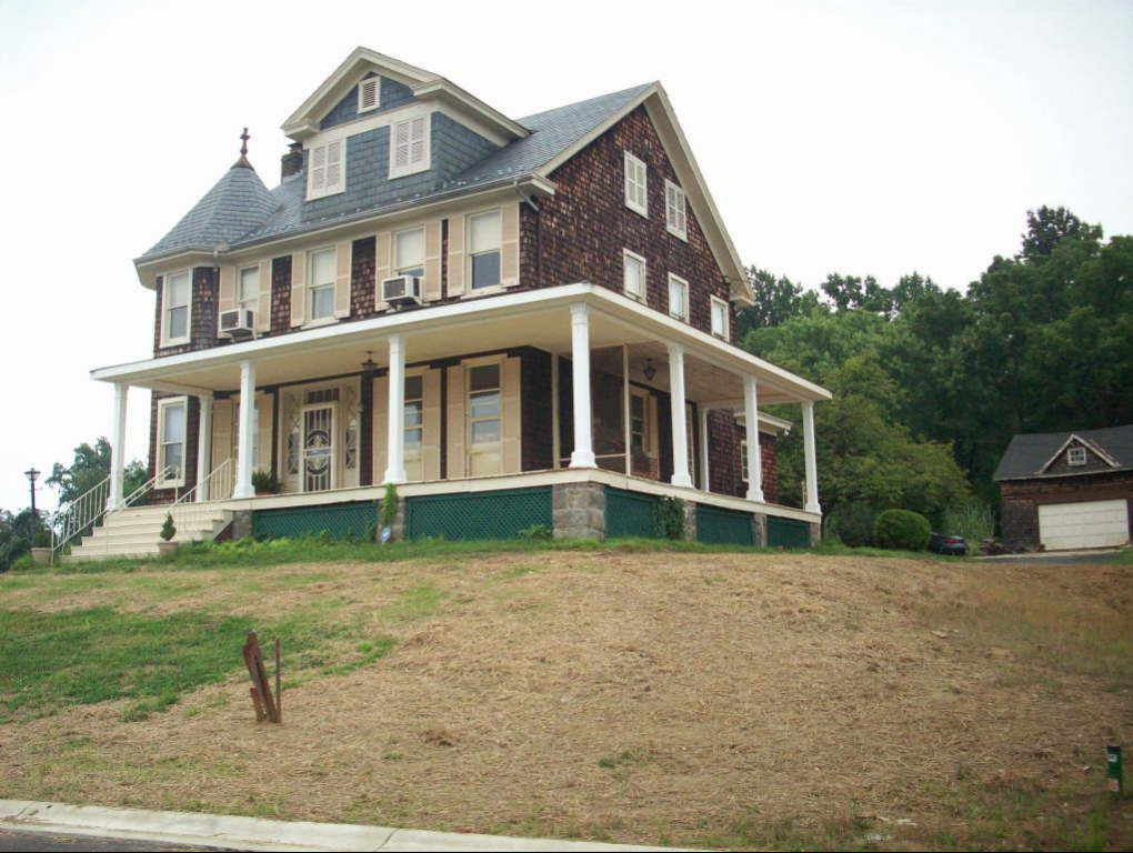 A large house sits on top of a grassy hill