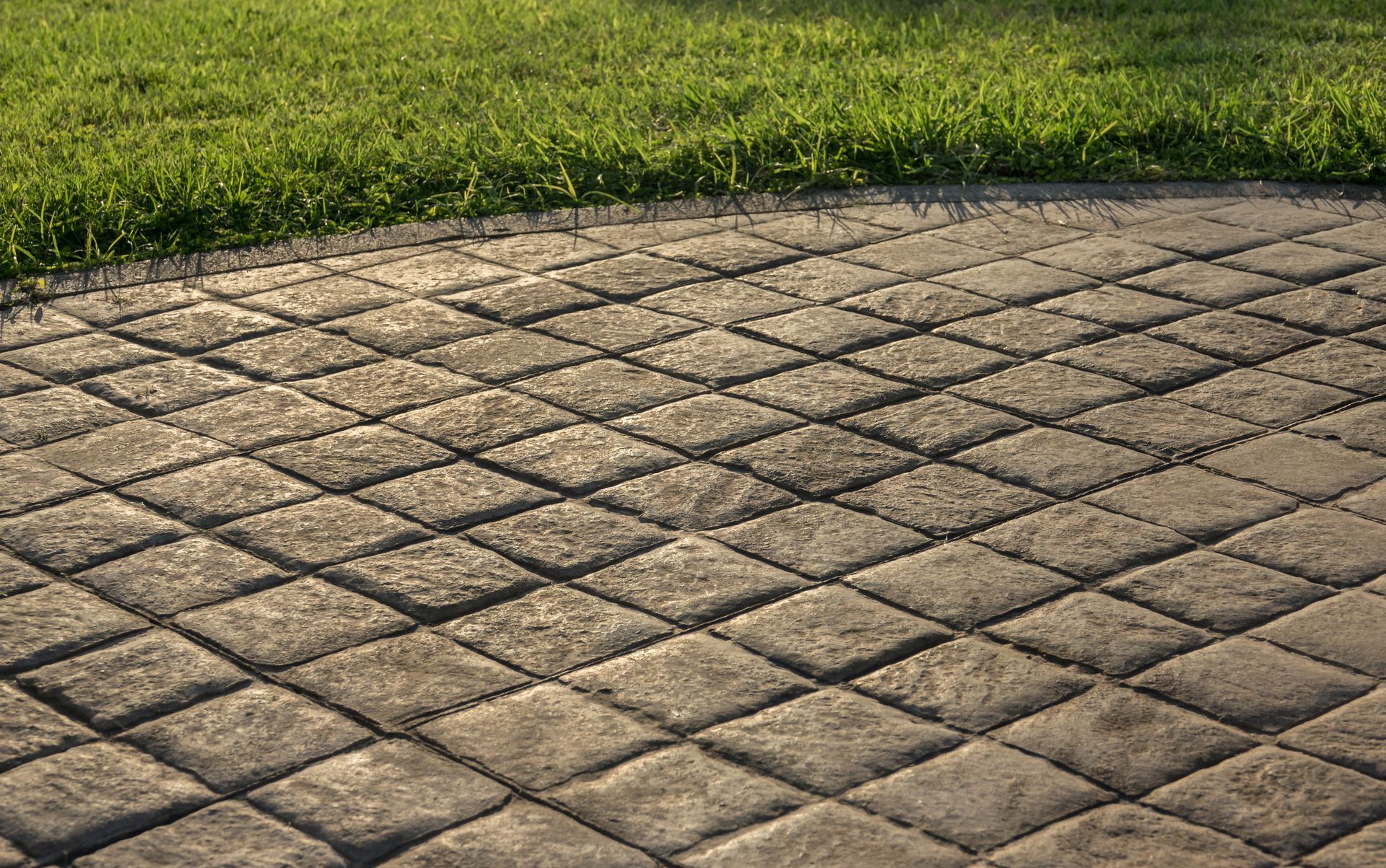A brick walkway next to a lush green field of grass.