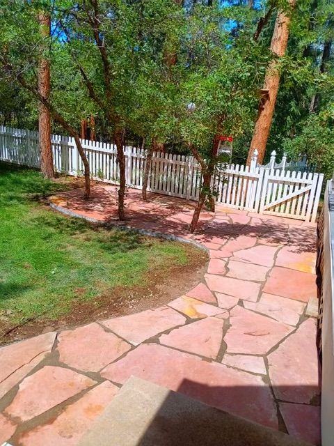 A stone patio with a white picket fence and trees in the background.