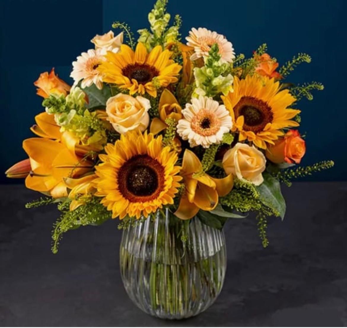 Sonnenblumen- und gelber Rosenstrauß in einer Glasvase vor dunklem Hintergrund