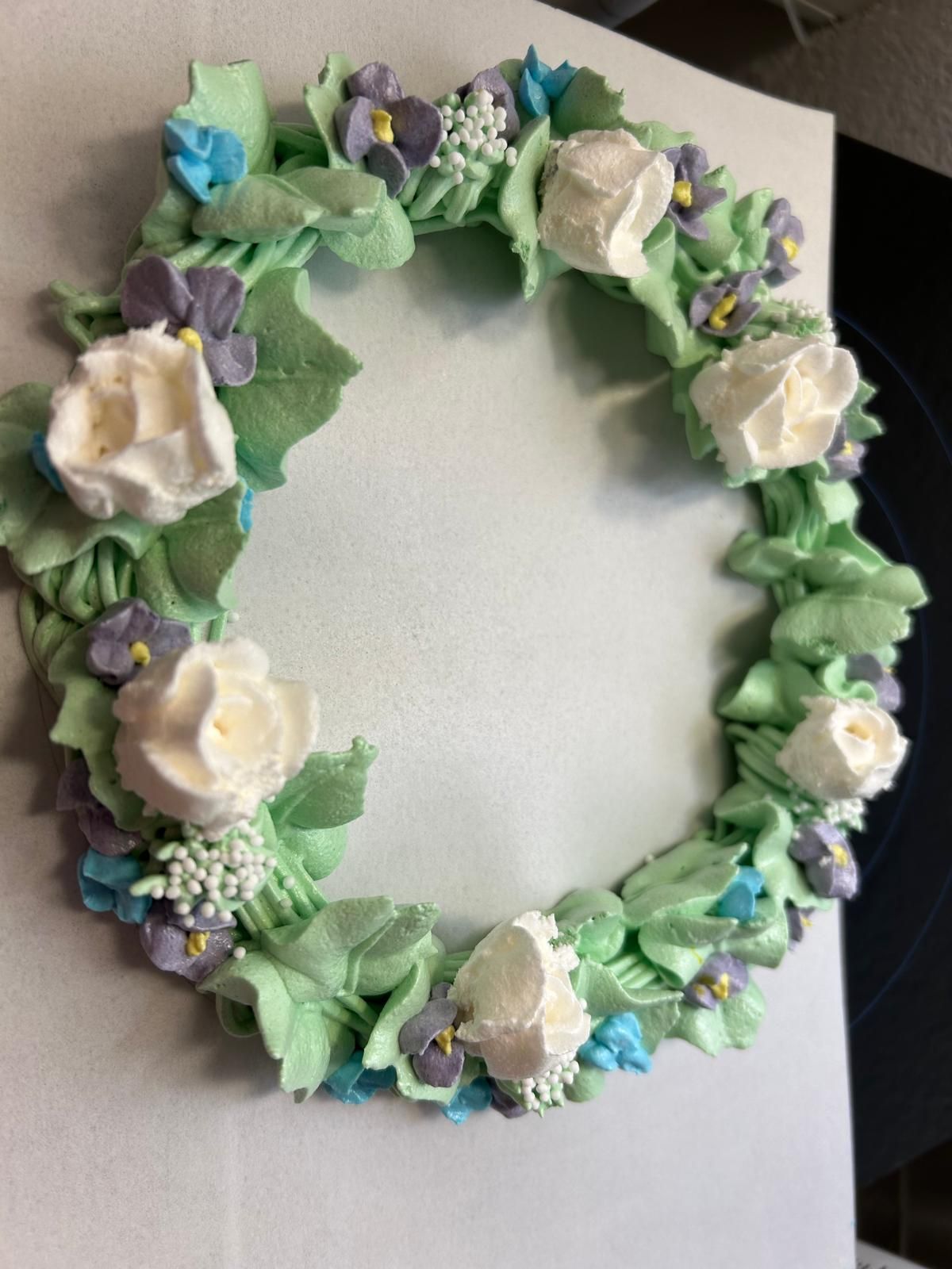 Blumenkranz mit weißen und violetten Blüten und grünem Band an einer hellen Wand