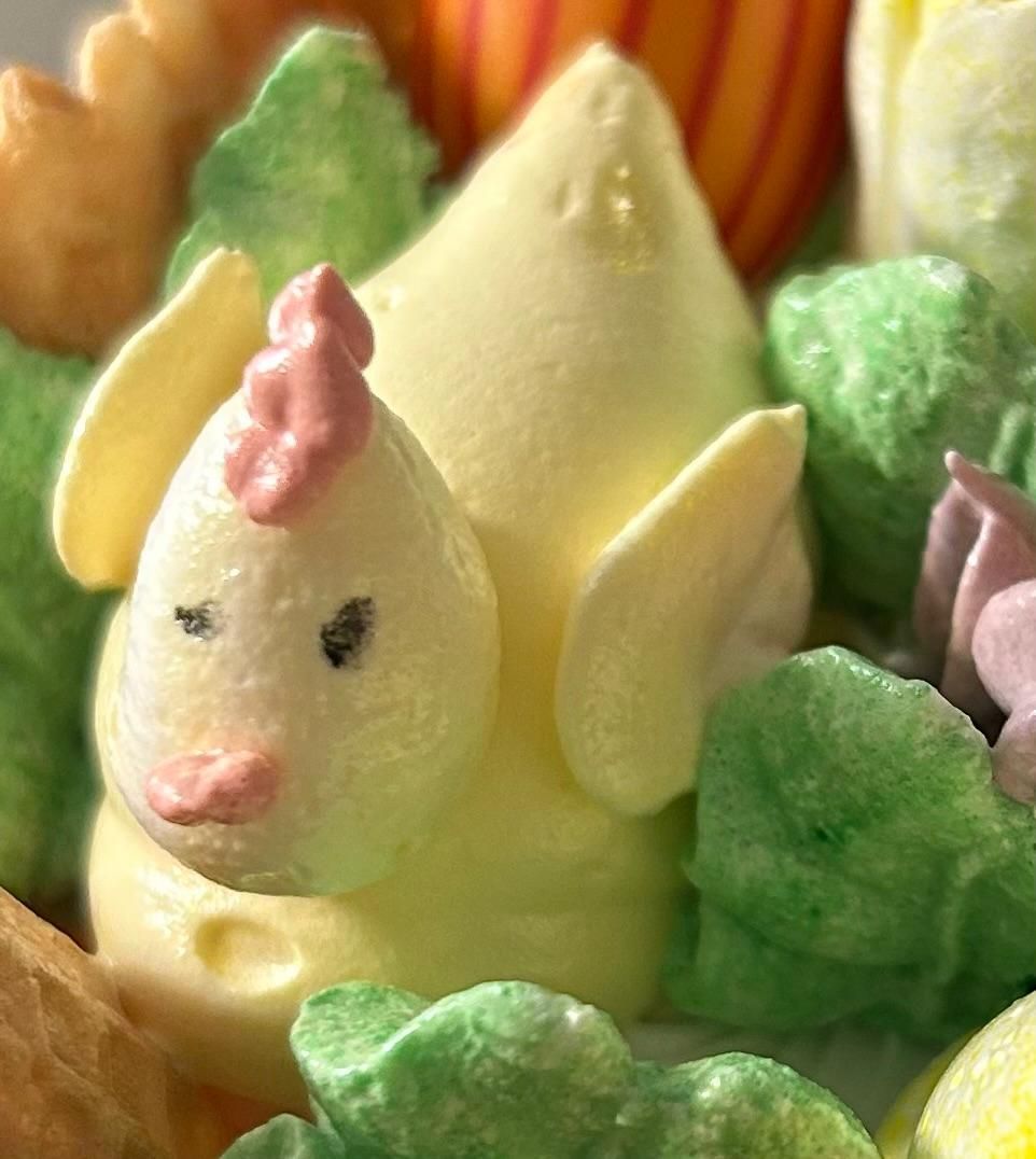 Gelbes, zuckerglasiertes, kükenförmiges Dessert mit rosa Schnabel und Kamm, umgeben von grünen und orangen Süßigkeiten
