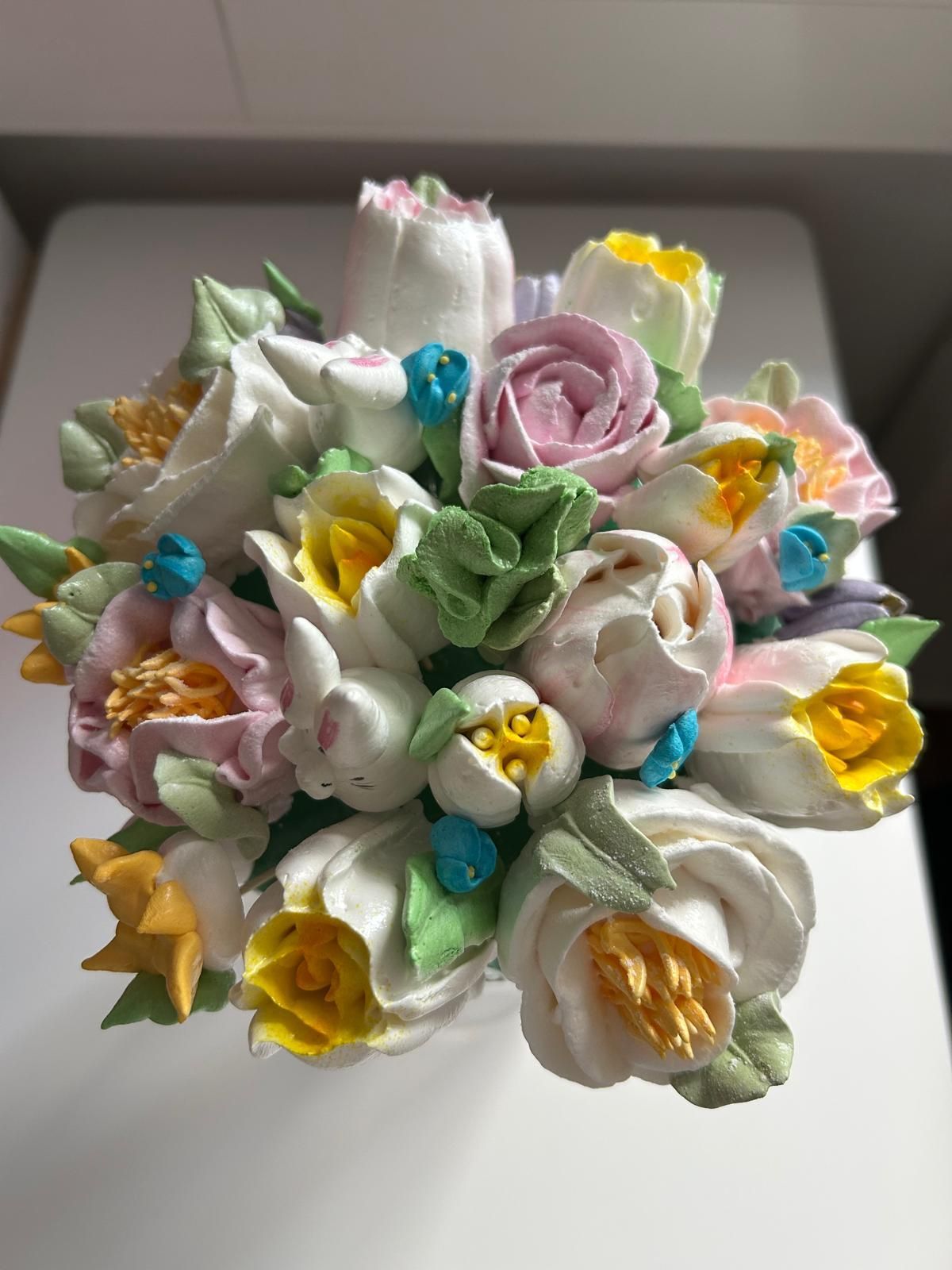 Ein Strauß aus pastellfarbenen künstlichen Blumen in Rosa, Weiß, Gelb und Grün auf weißem Untergrund