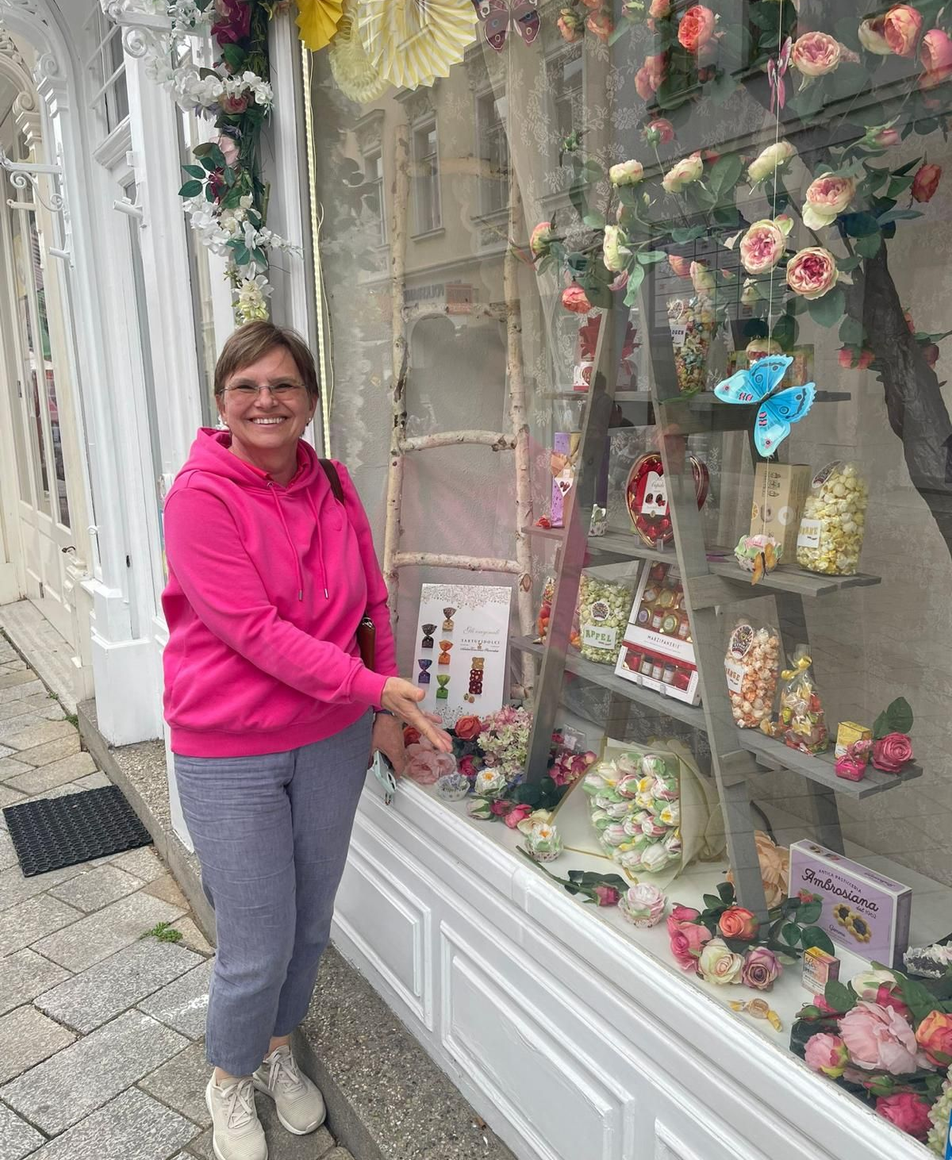 Frau steht vor einem Schaufenster und zeigt auf essbare Blumensträuße