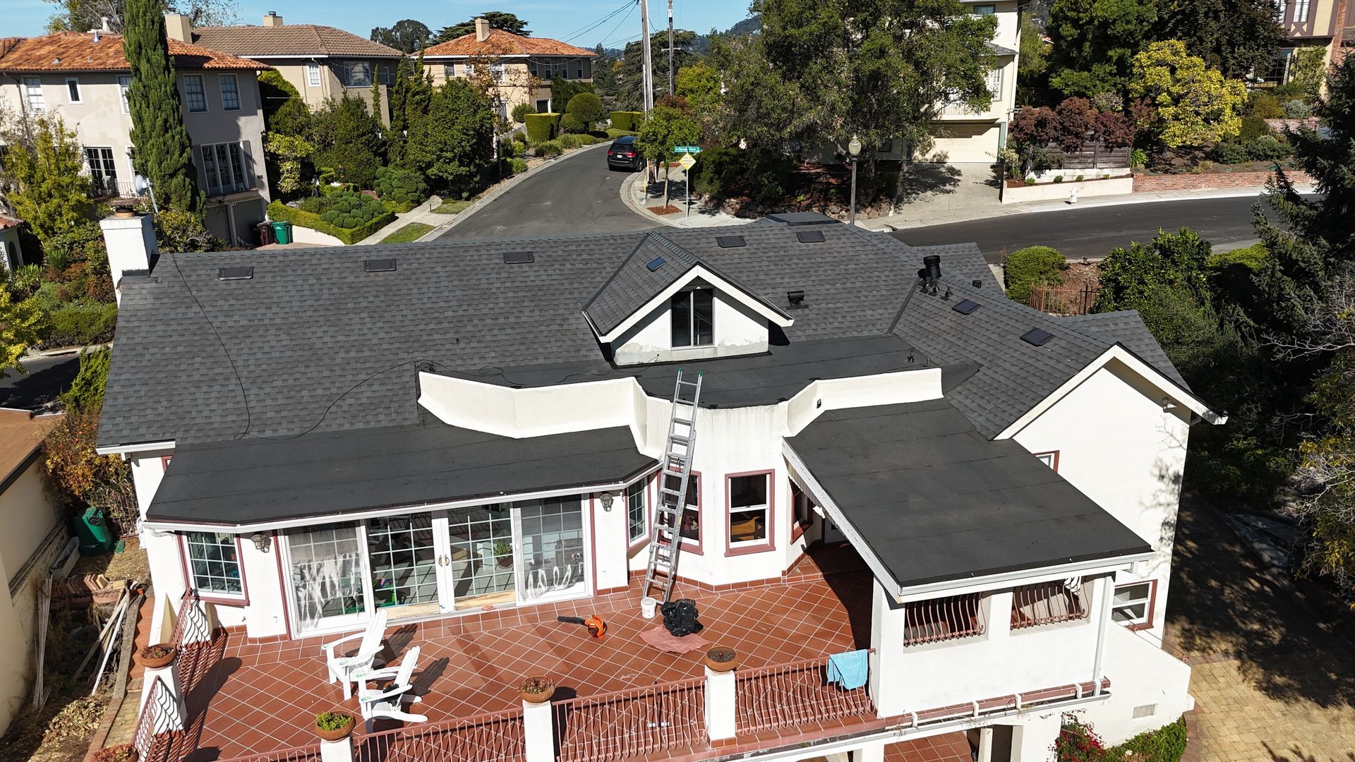 House with gray roof and red deck, surrounded by trees and street, sunny day.