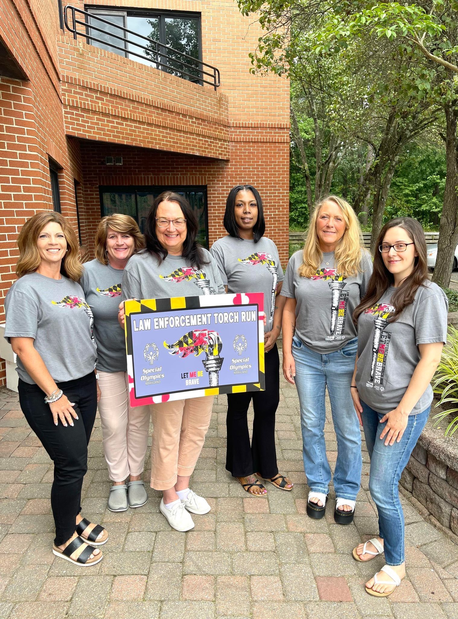 A group of women are standing in front of a brick building holding a sign.