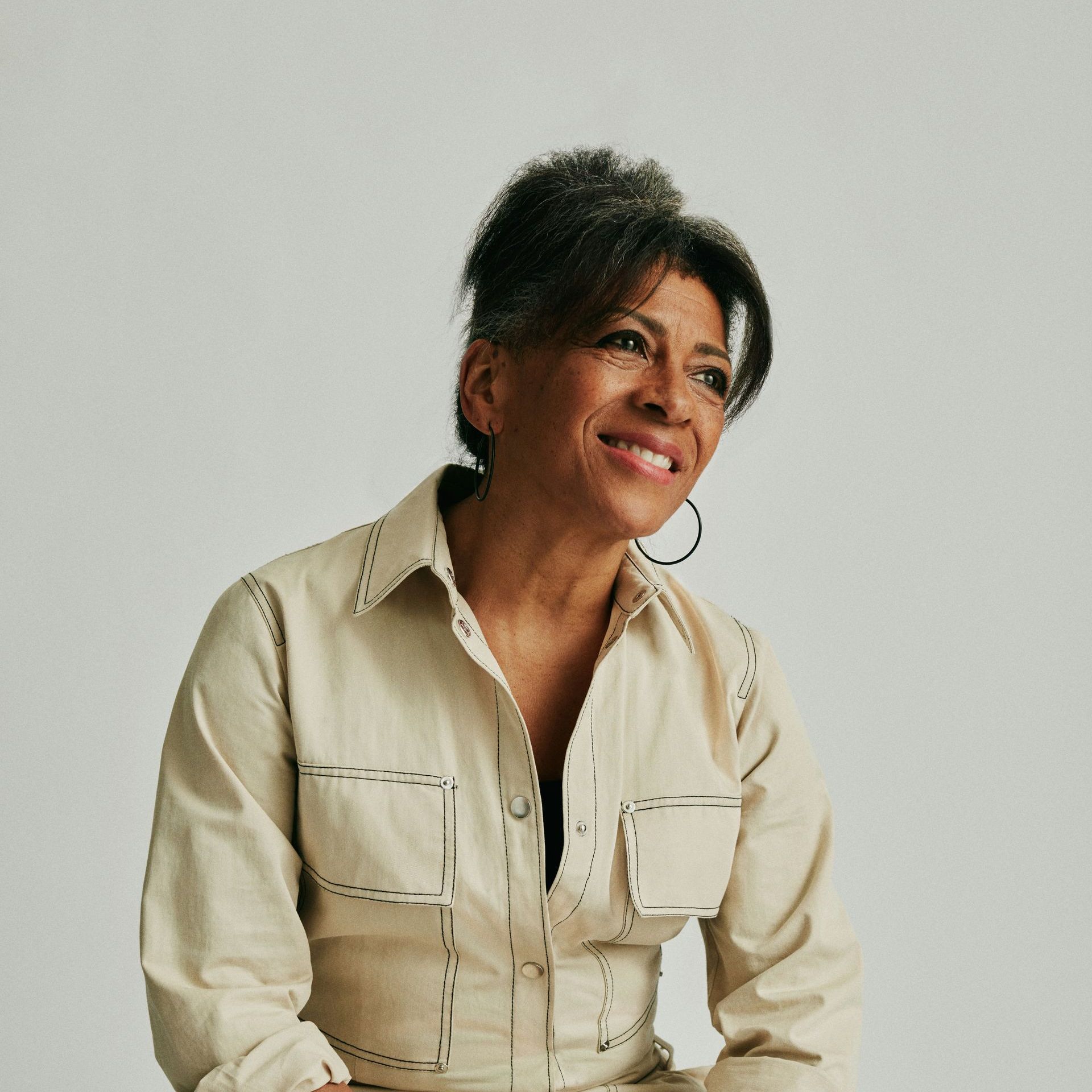 A woman wearing a white shirt and hoop earrings is smiling
