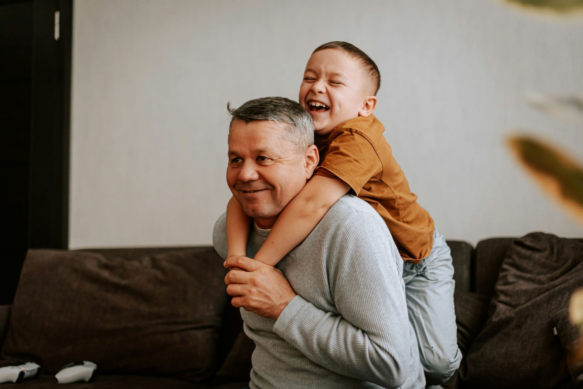 A man is giving a boy a piggyback ride while sitting on a couch.