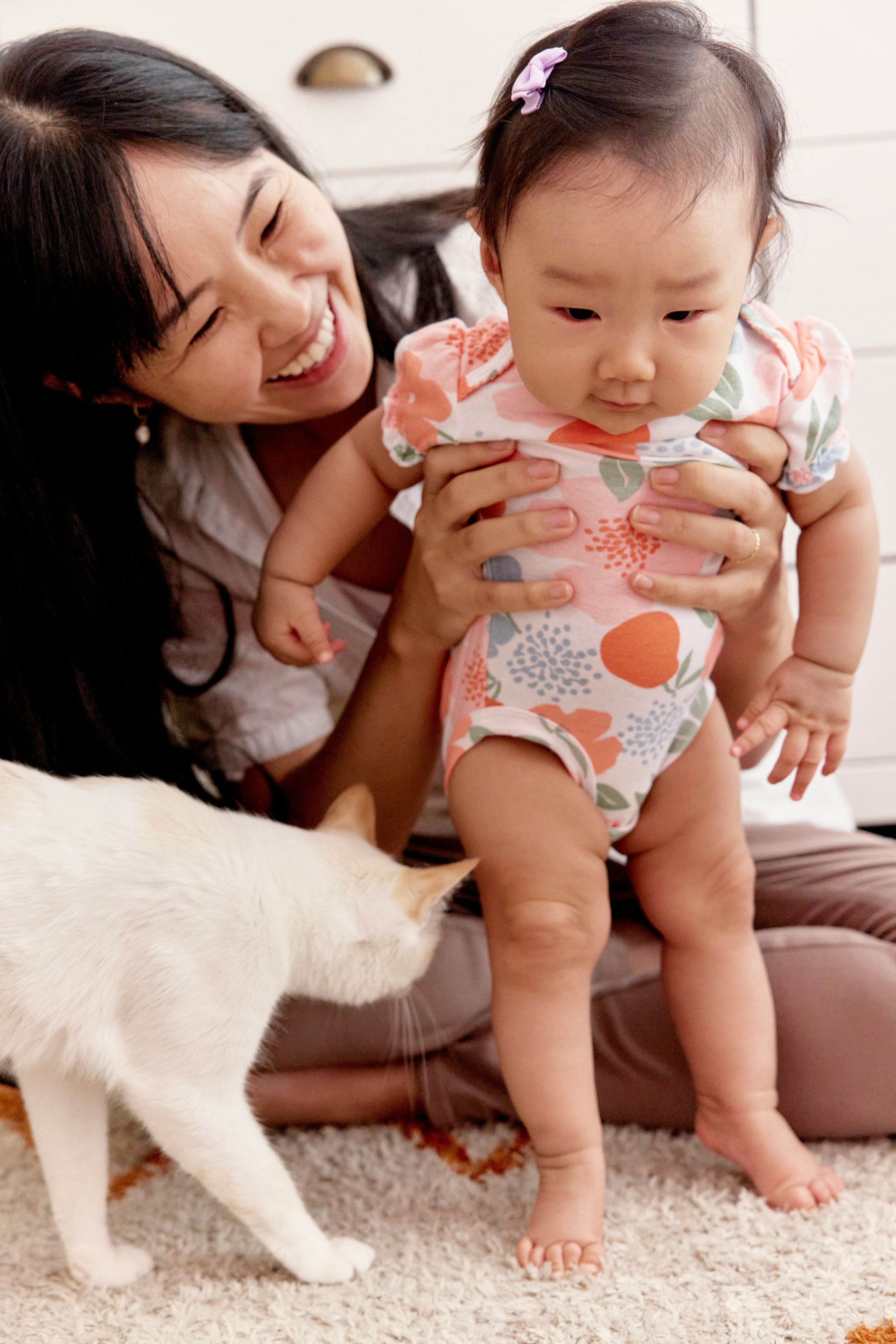 A woman is holding a baby and a cat is looking at the baby.