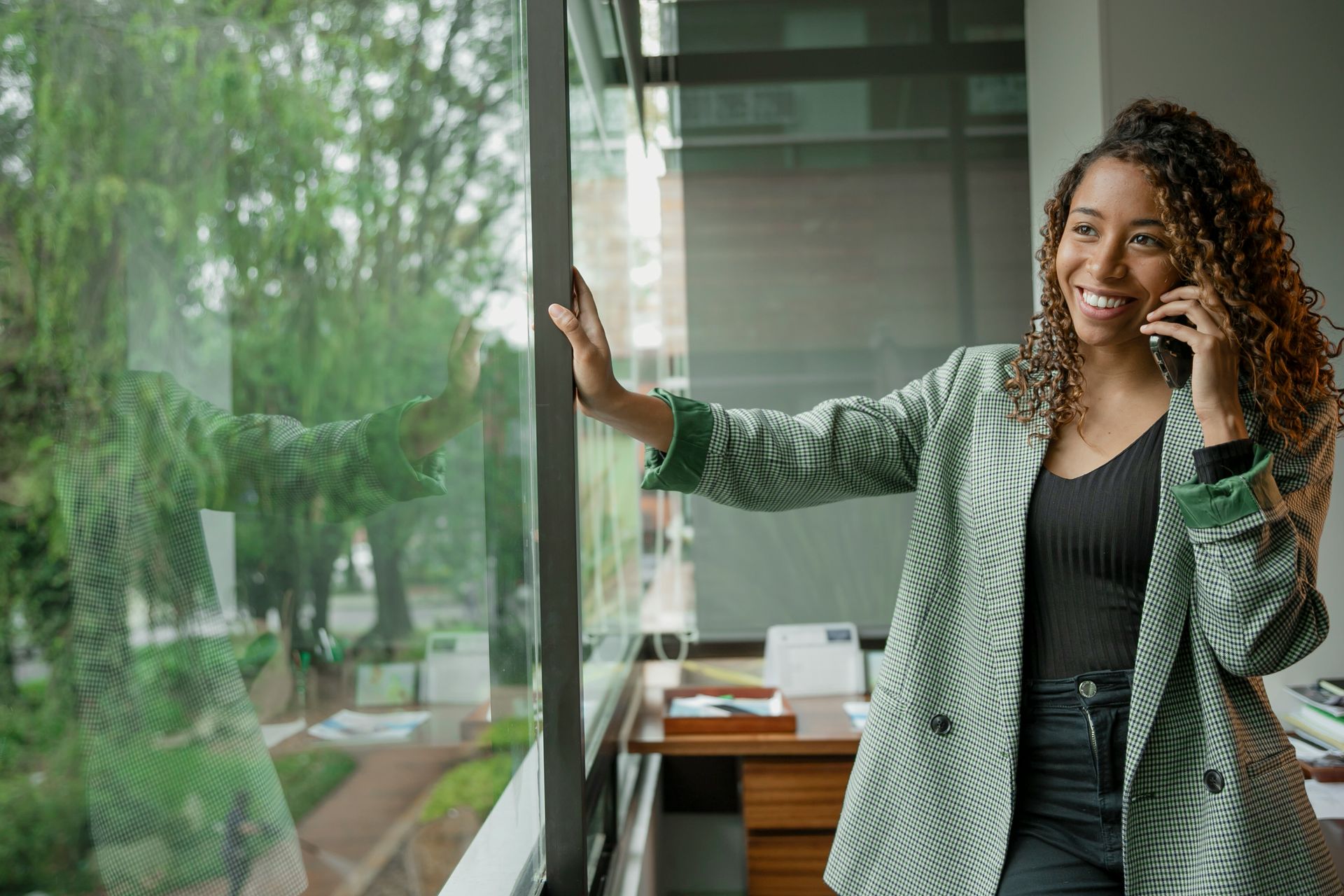 A woman is standing in front of a window talking on a cell phone.