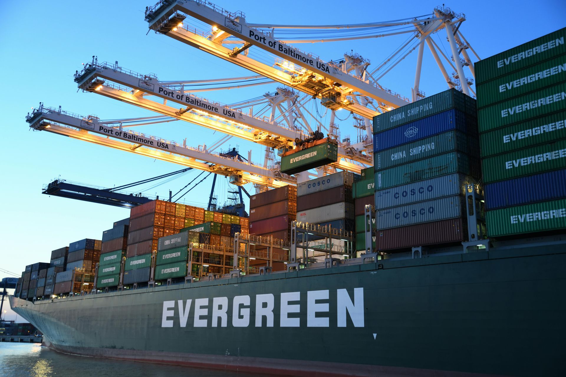 A large evergreen container ship is docked at a port.