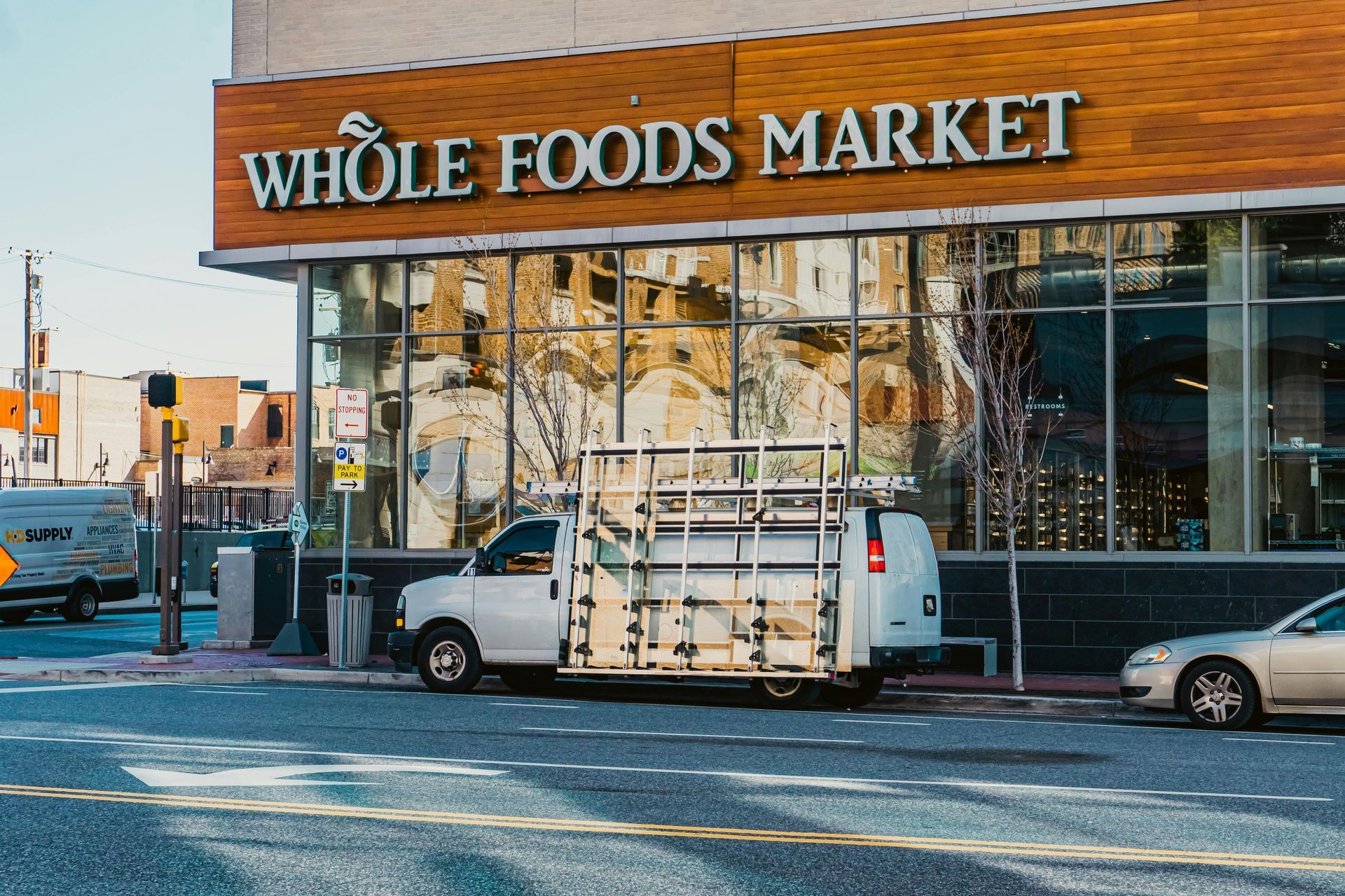 A white van is parked in front of a whole foods market.