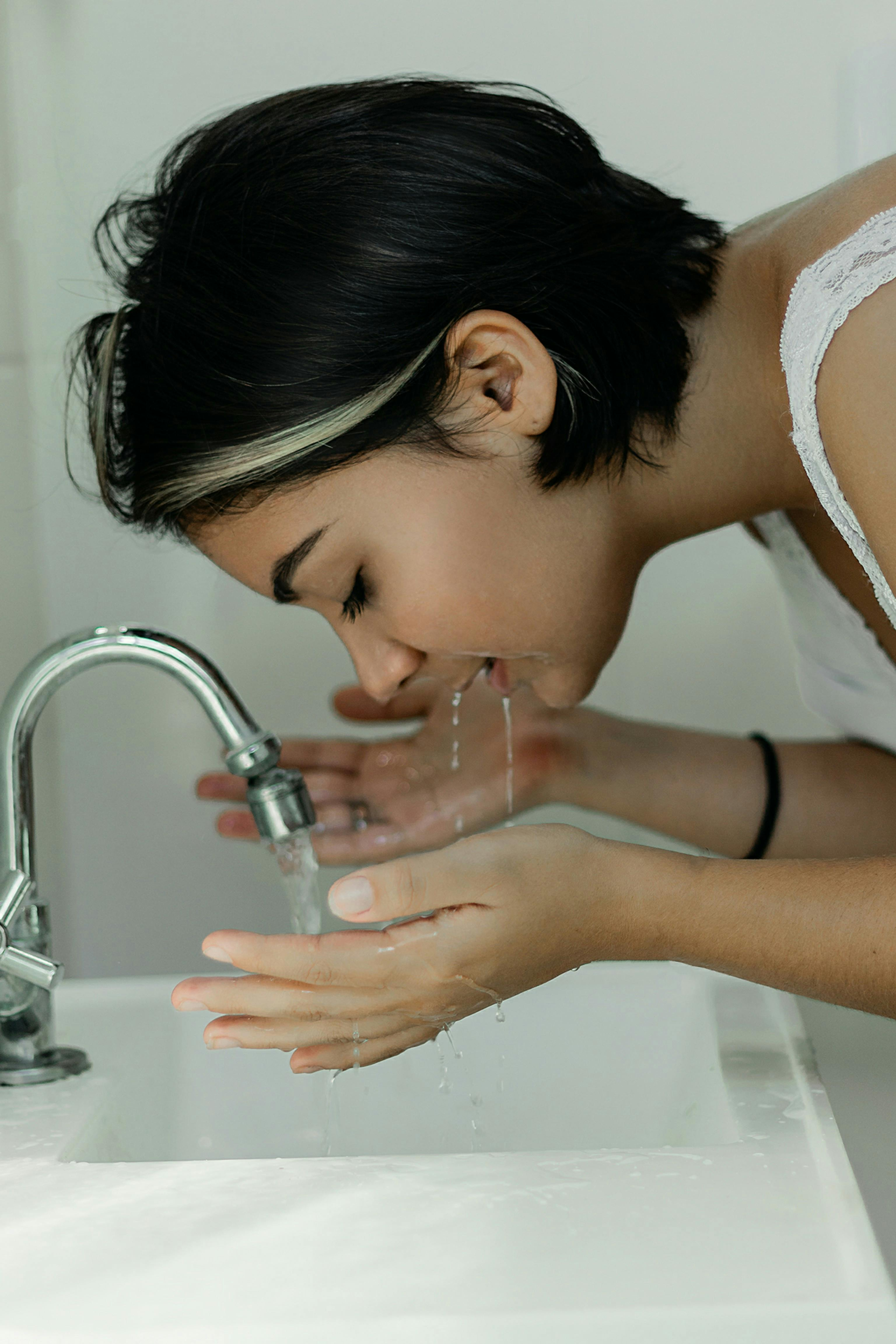 A woman is washing her face in a bathroom sink.