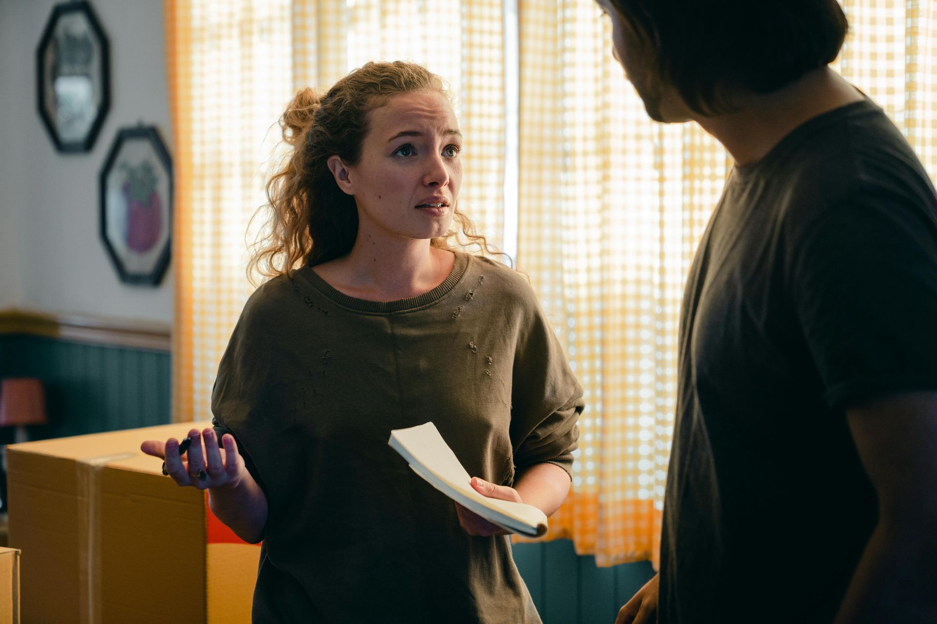A woman is holding a piece of paper while talking to a man in a living room.