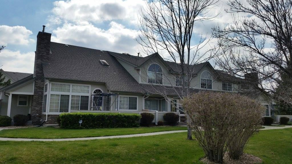 A multi-unit suburban townhouse complex with gray siding, shingled roofs, stone chimneys, and front lawns.